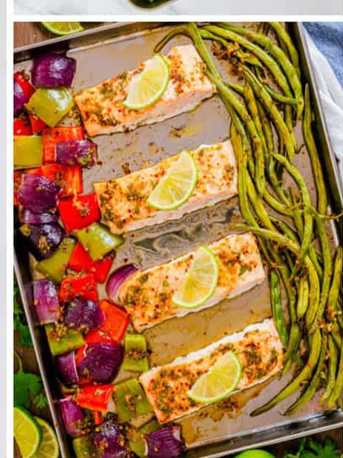 Baked salmon filets with roasted vegetables and lime slices on a sheet pan.