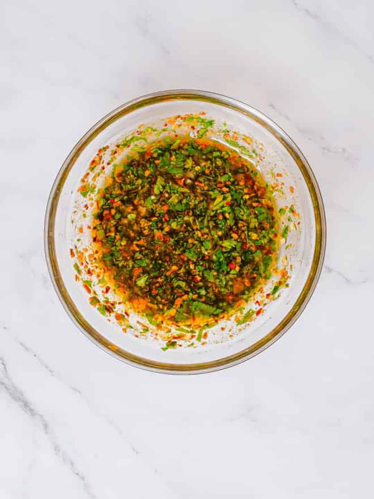 Lime garlic marinade with parsley and chili flakes whisked together in a glass bowl.