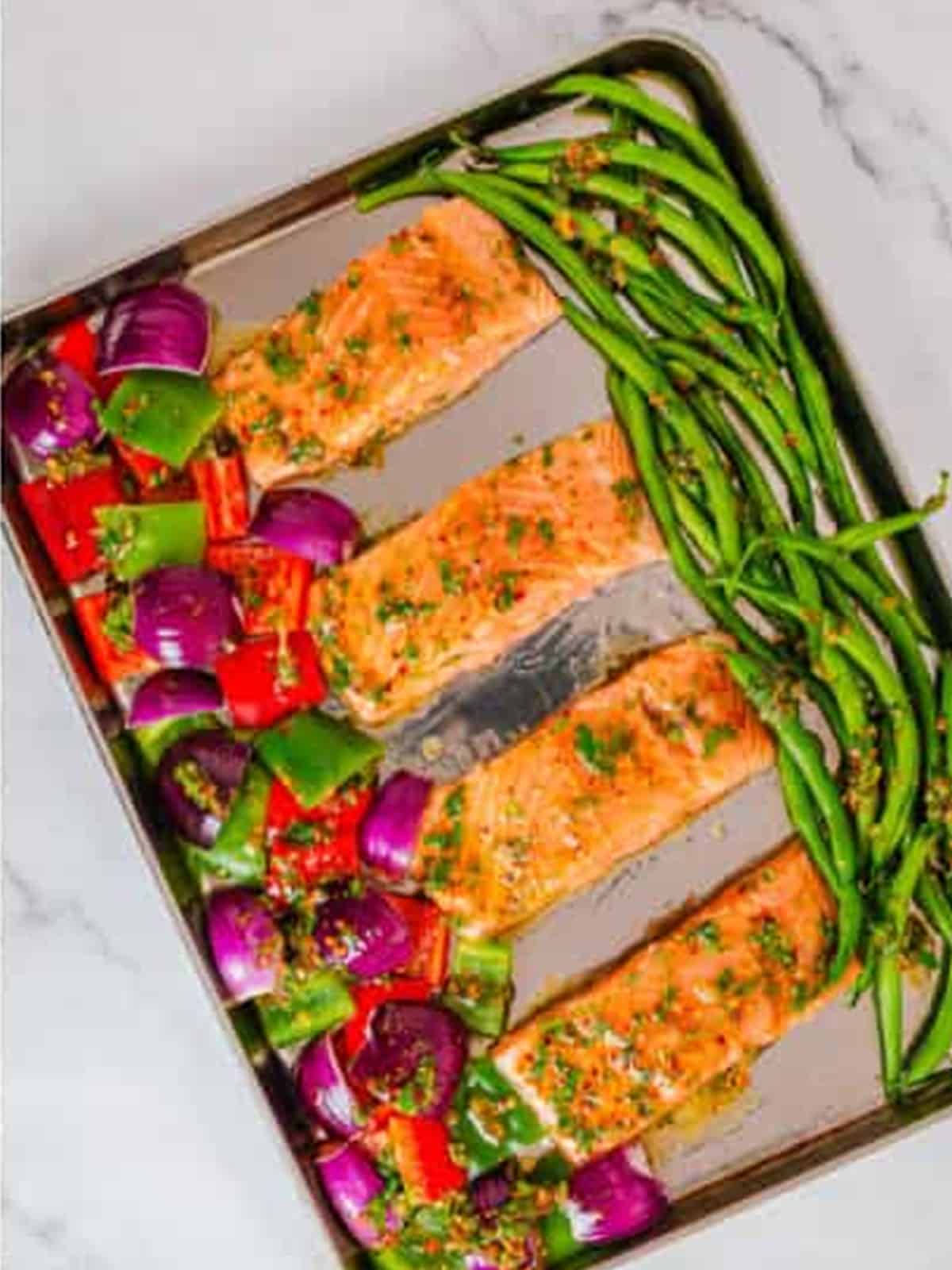 Raw salmon filets with peppers, red onion, and green beans arranged on a sheet pan.
