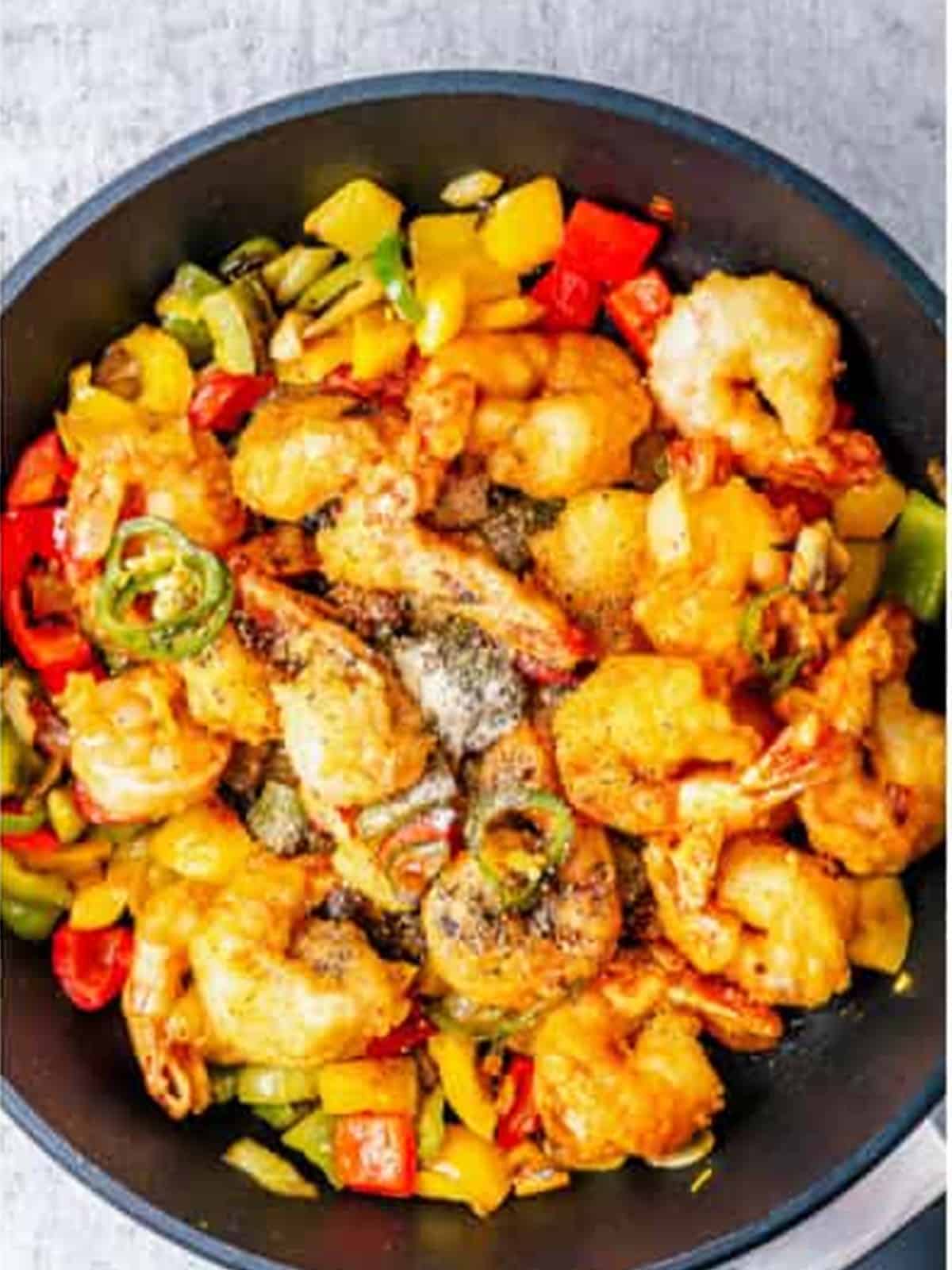 Finished crispy salt and pepper shrimp with peppers in a skillet.