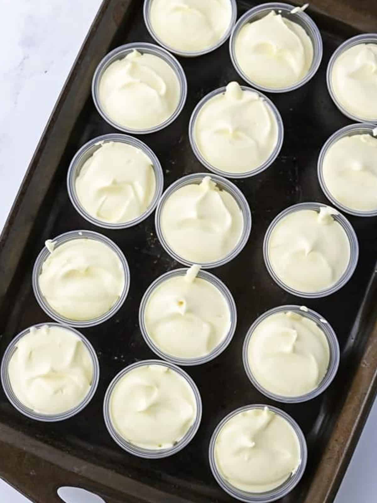 Two ounce shot cups filled with salted caramel pudding shot mixture on a tray for chilling.