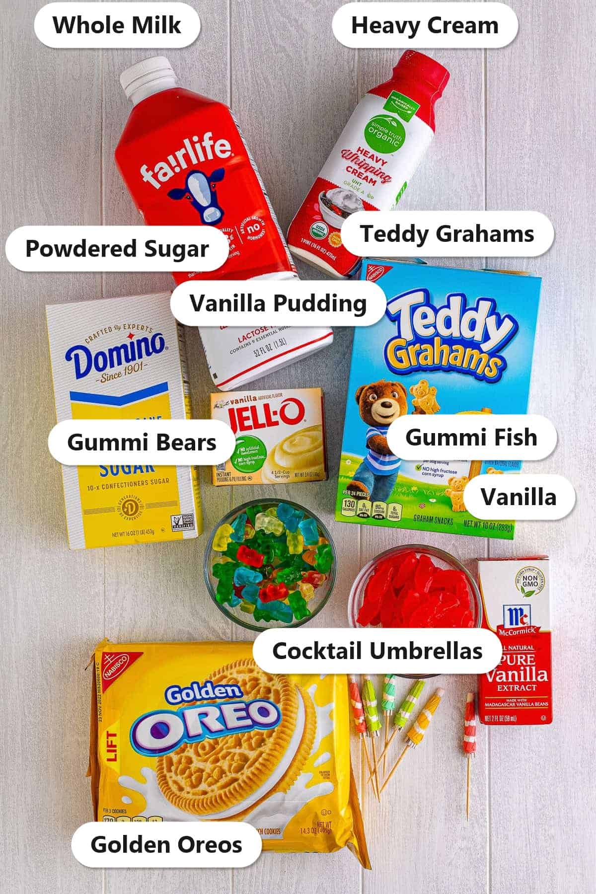 Labeled ingredients for sand pudding including golden Oreos, instant vanilla pudding, whole milk, heavy cream, powdered sugar, vanilla, and gummi candy garnishes.