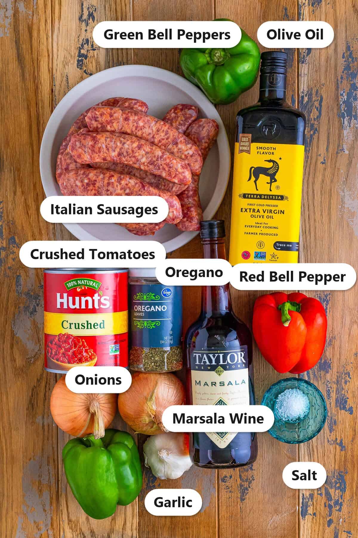 Labeled ingredients to make sausage and peppers recipe including Italian sausages, bell peppers, onions, garlic, crushed tomatoes, oregano, olive oil, salt, and Marsala wine.