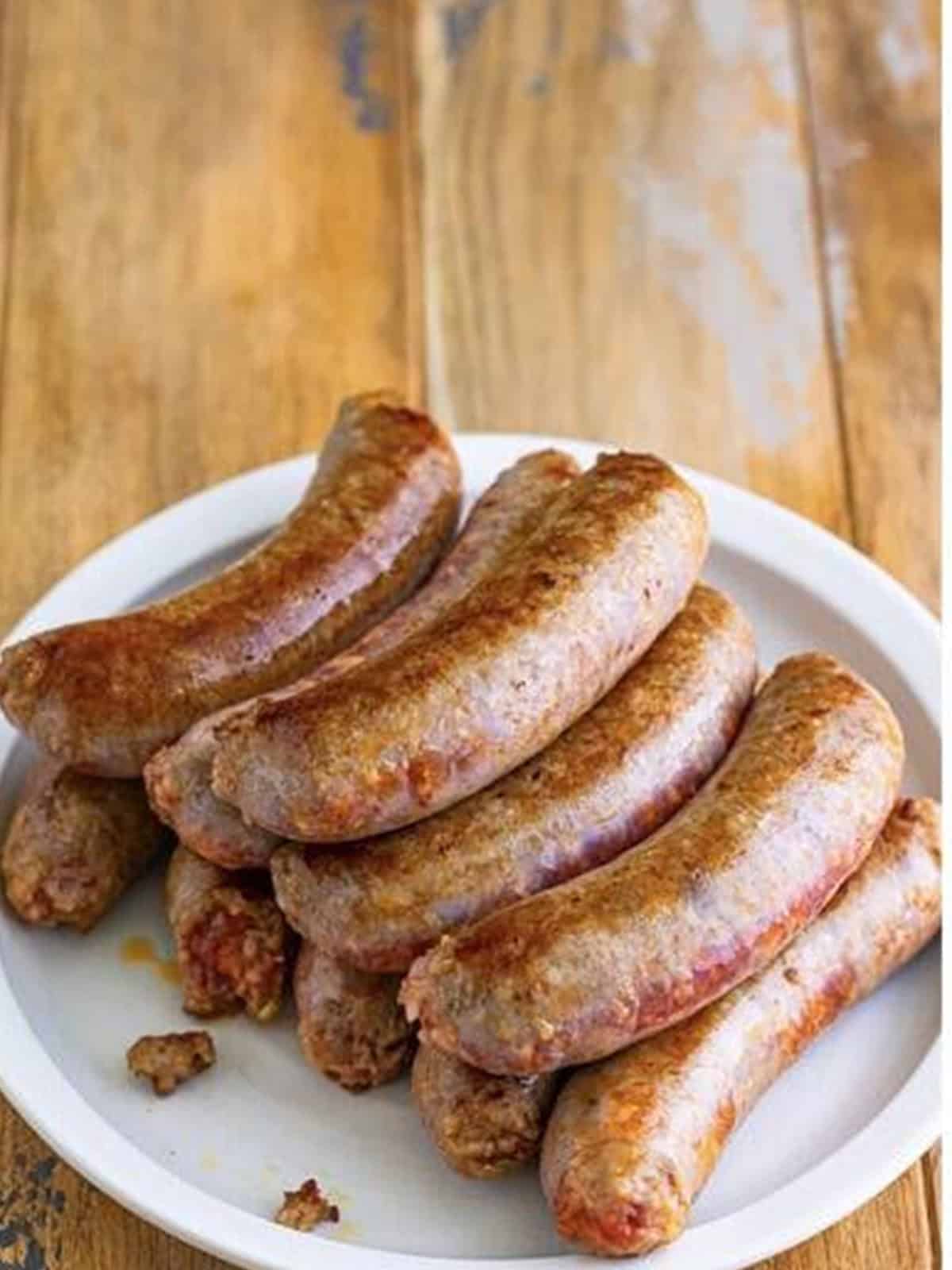 Browned Italian sausages resting on a white plate for sausage and peppers recipe.