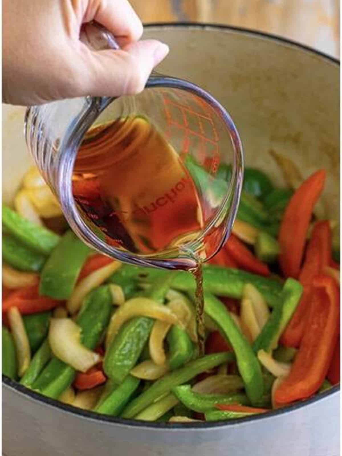 Marsala wine being poured over sauteed bell peppers and onions in a Dutch oven.