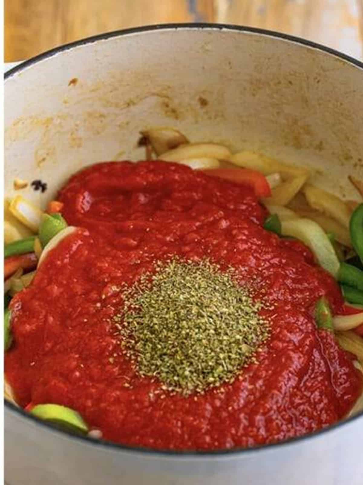Crushed tomatoes and dried oregano added on top of the peppers and onions in the pot.
