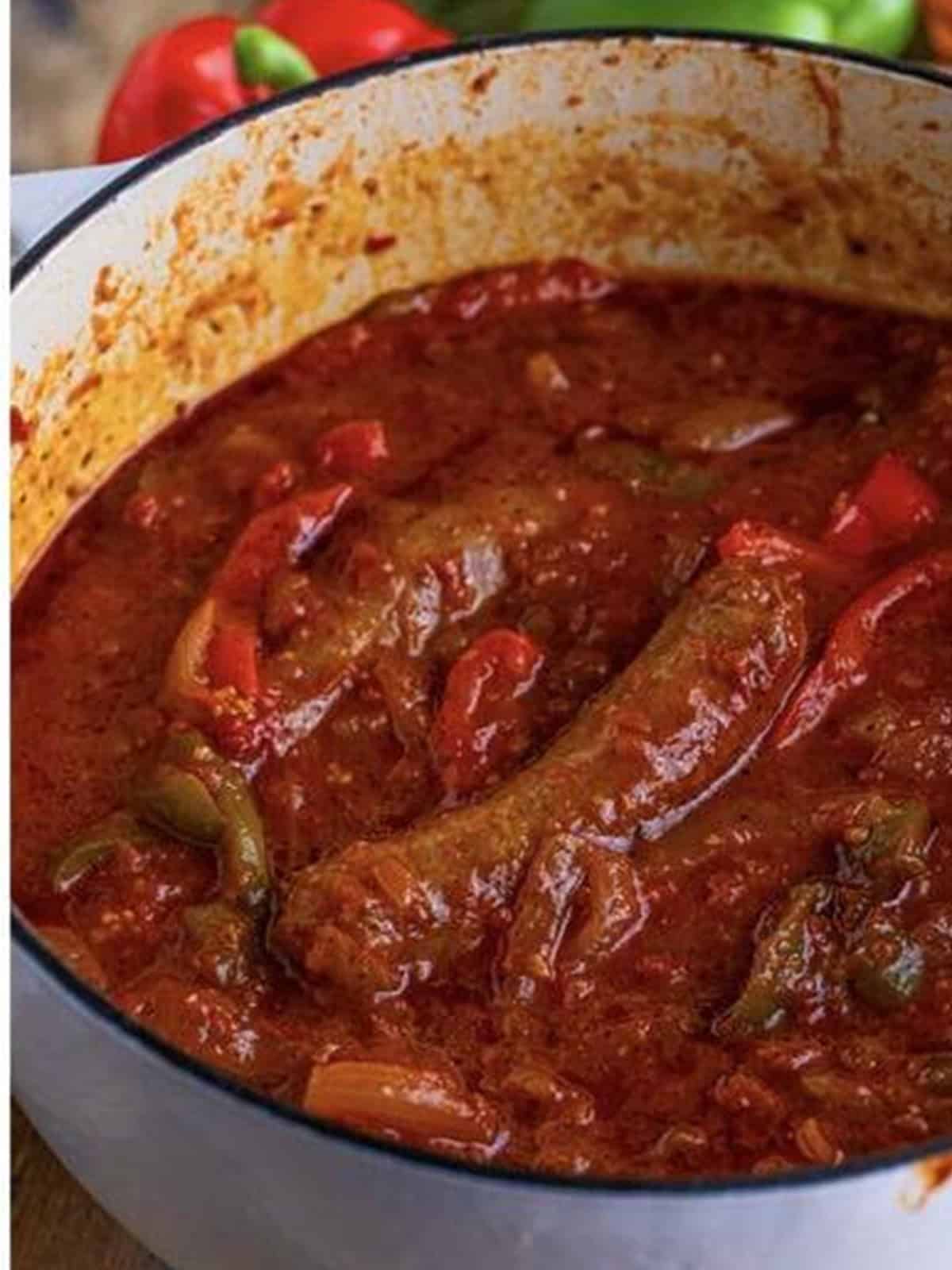 Finished sausage and peppers simmering in marsala tomato sauce in a Dutch oven.
