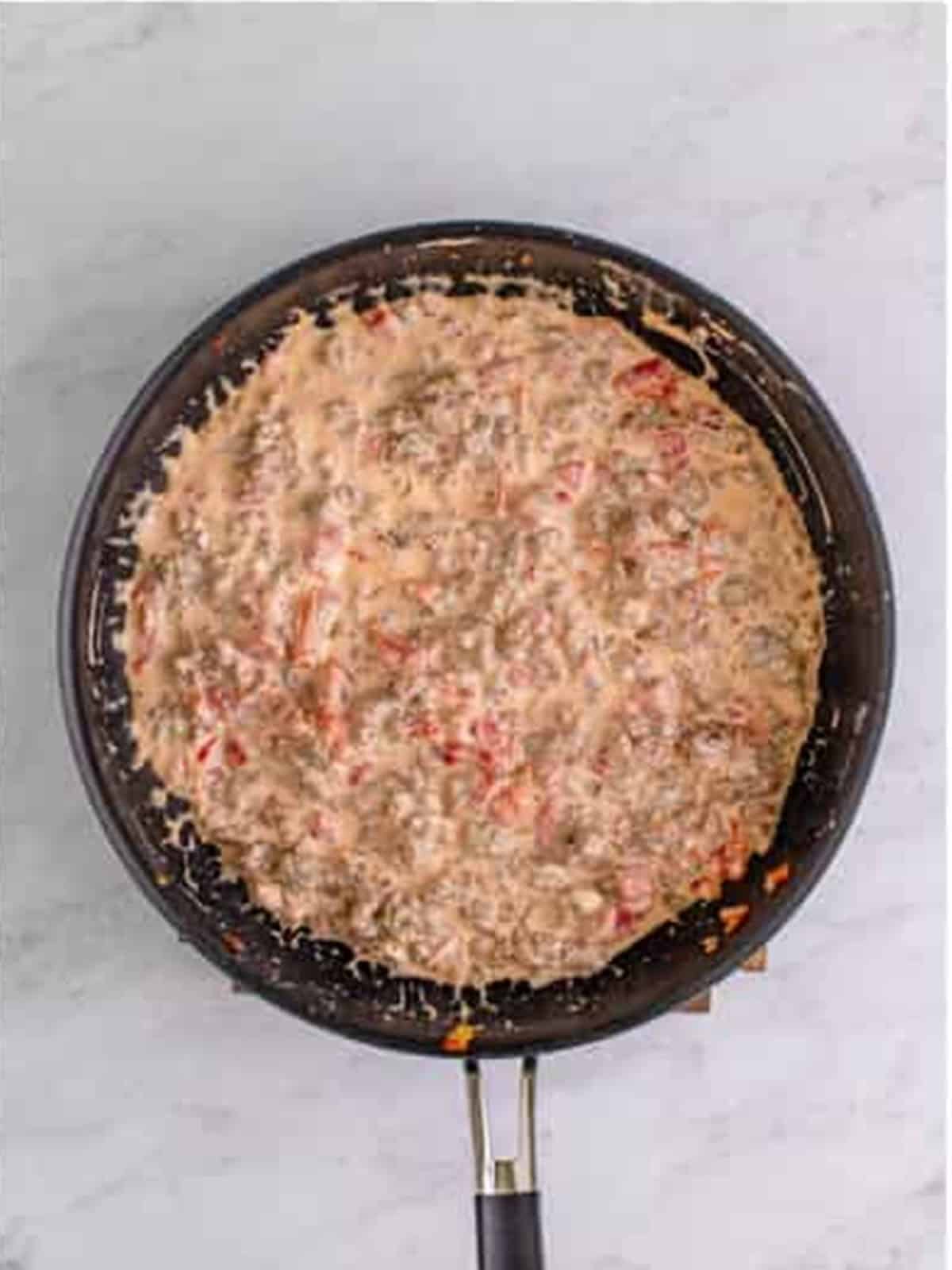 Creamy sausage dip with cream cheese and Rotel mixed in a skillet.