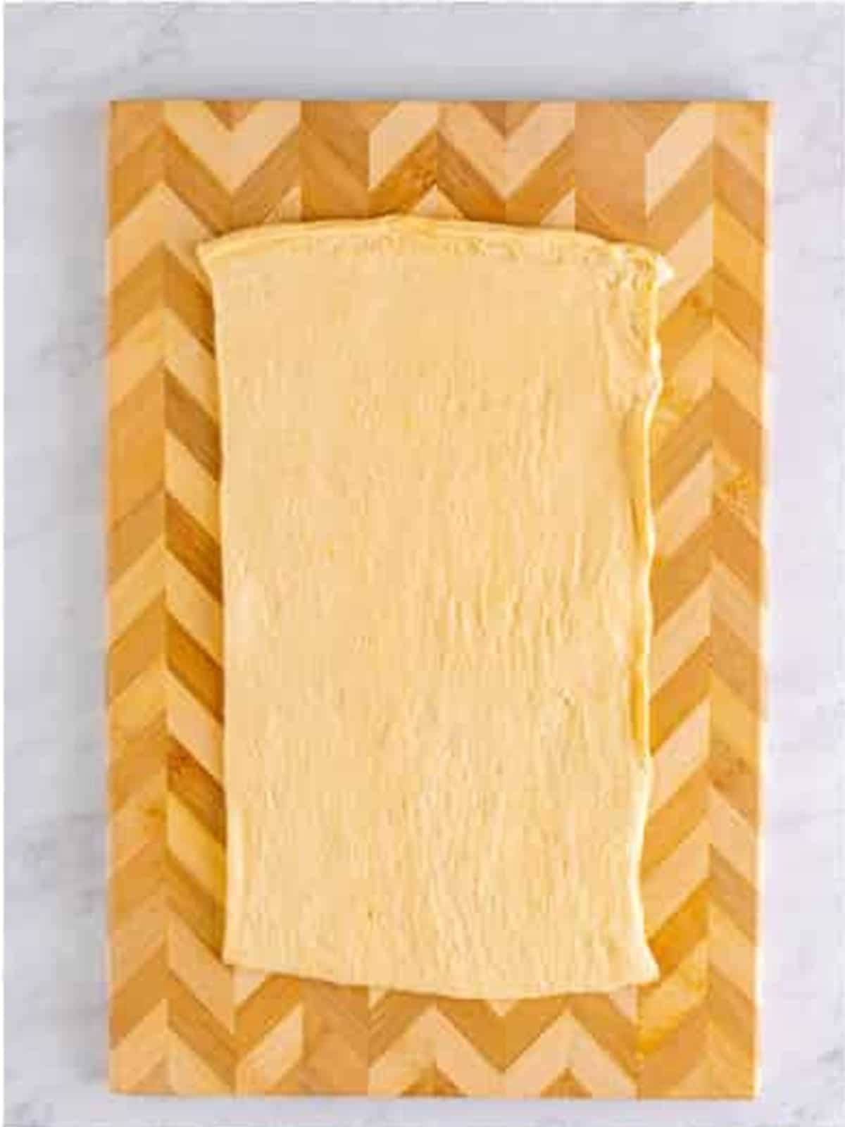 A crescent roll dough sheet rolled out on a work surface for sausage pinwheels.