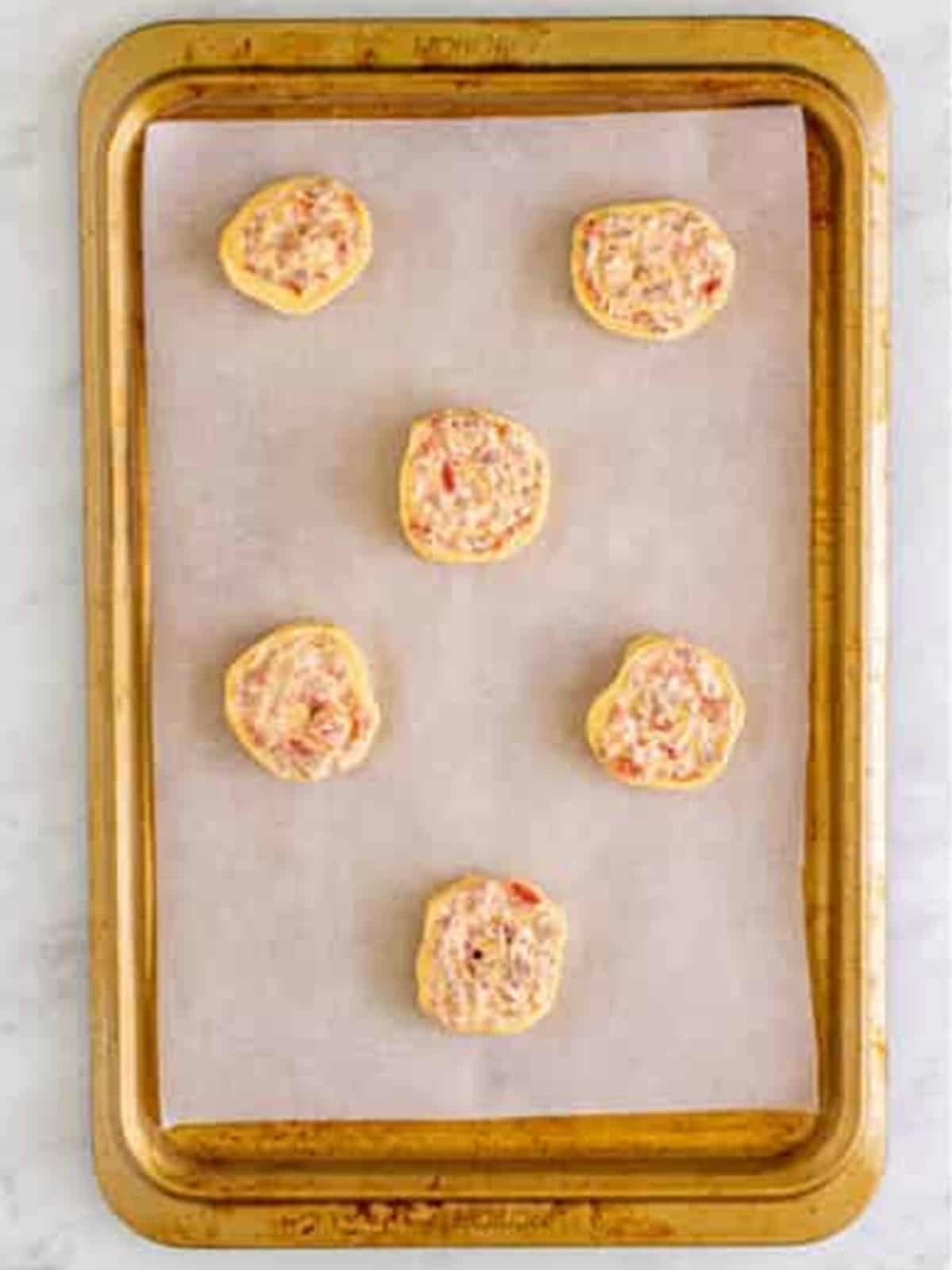 Sausage pinwheels arranged on a parchment lined baking tray.