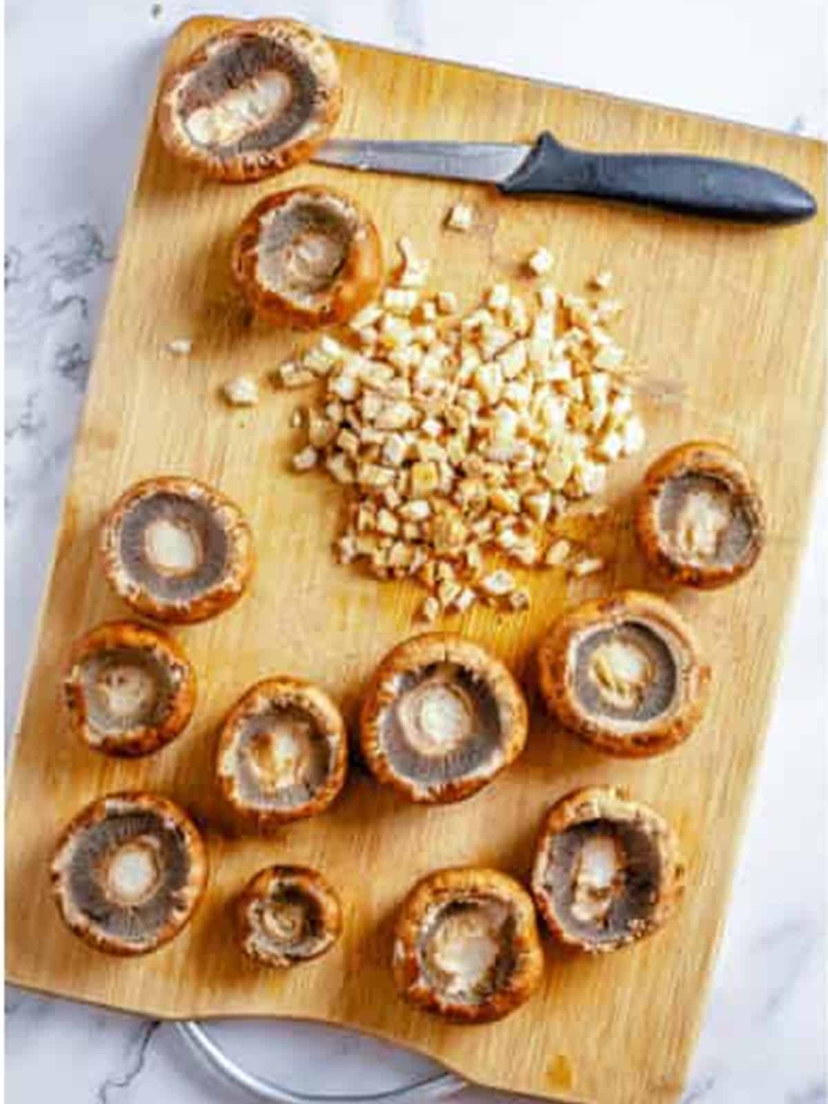 Cleaned baby bella mushroom caps with the stems removed and finely chopped on a board.