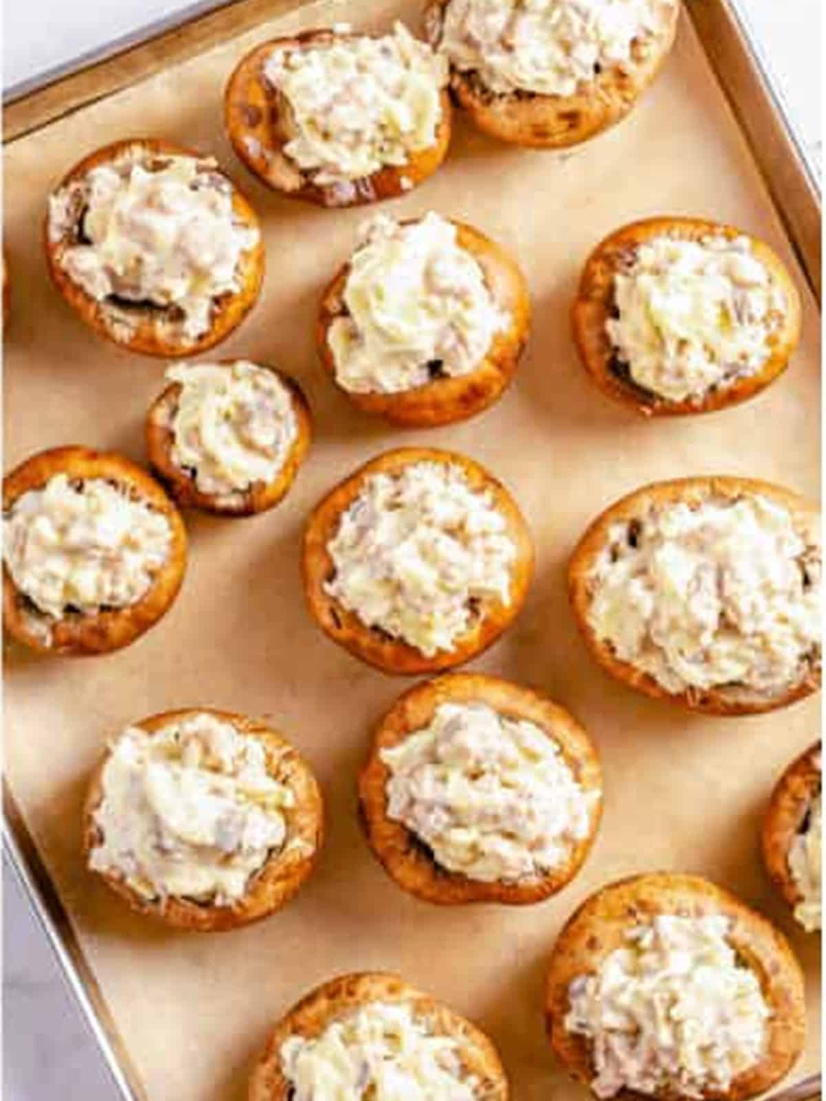 Mushroom caps stuffed with heaping sausage cream cheese filling on a baking sheet.
