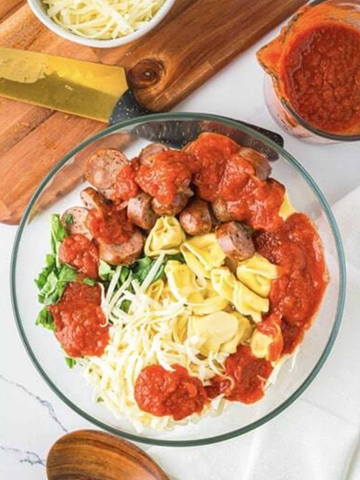 Tortellini, sliced sausage, marinara, mozzarella, and basil combined in a large mixing bowl.