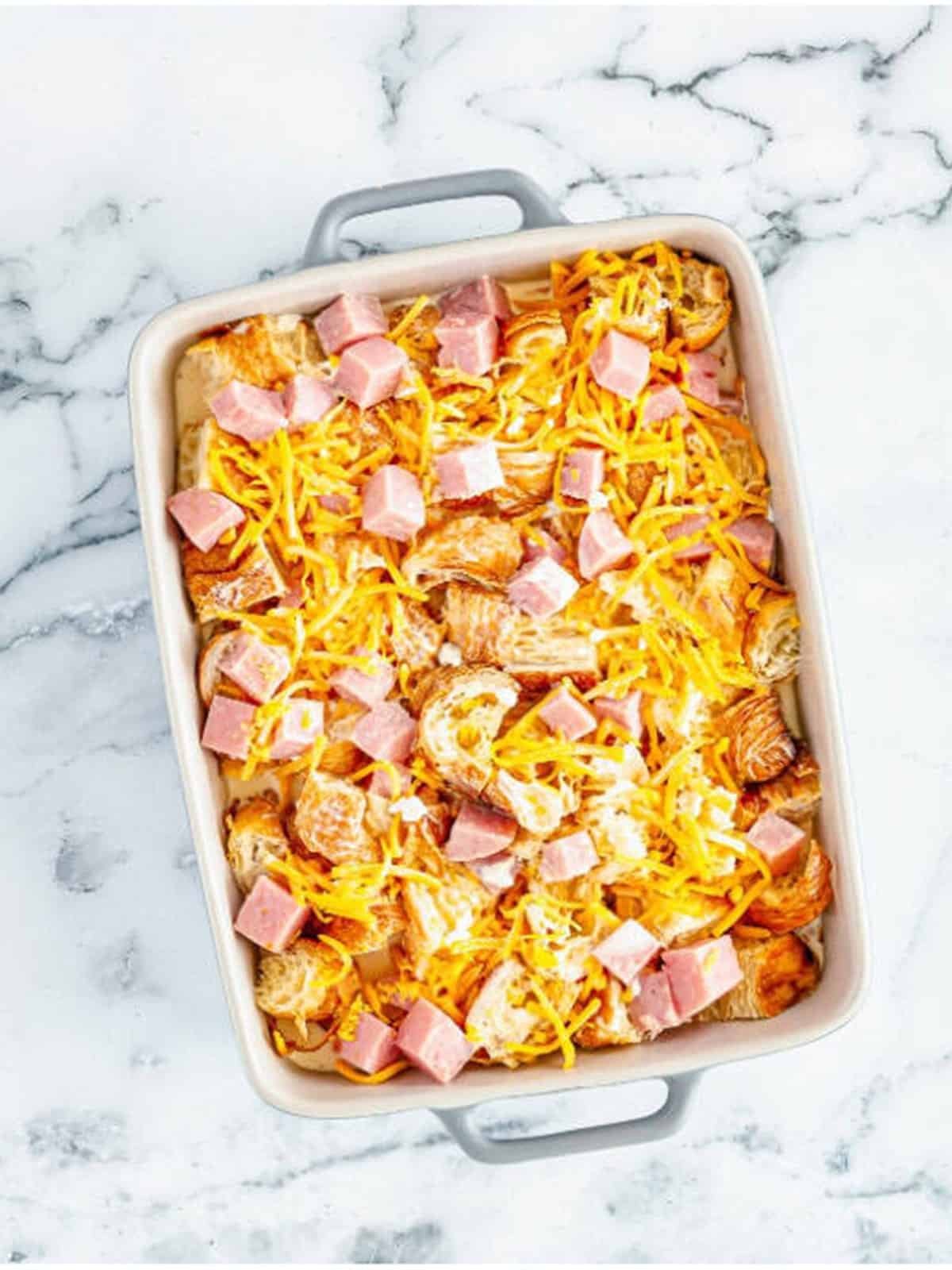 Egg custard poured over layered croissants, ham, and cheese in a baking dish.