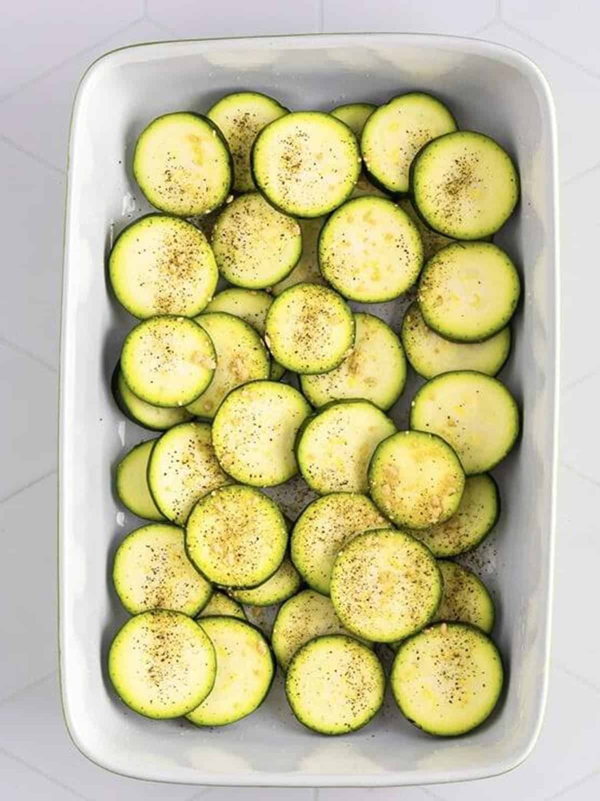 Sliced zucchini rounds layered and seasoned in a baking dish.