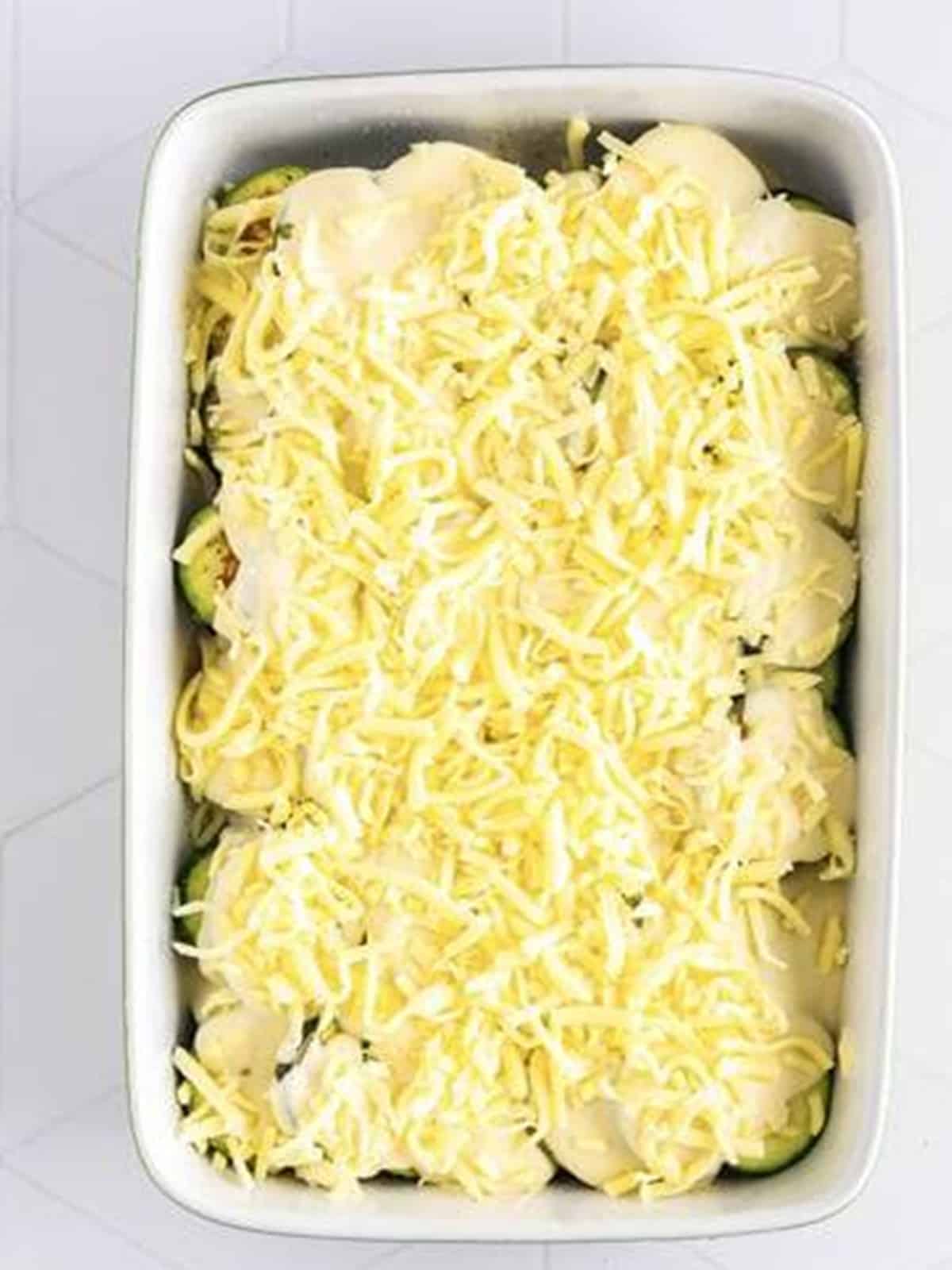 Scalloped zucchini topped with shredded Italian cheese before baking.