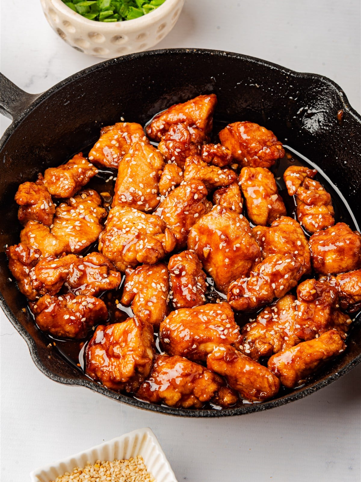 Finished glazed sesame chicken in the skillet topped with sesame seeds and green onions.