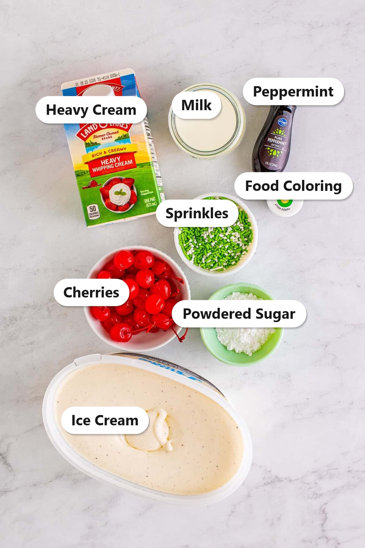Labeled ingredients for a shamrock shake including heavy cream, milk, peppermint extract, food coloring, sprinkles, cherries, powdered sugar, and ice cream.