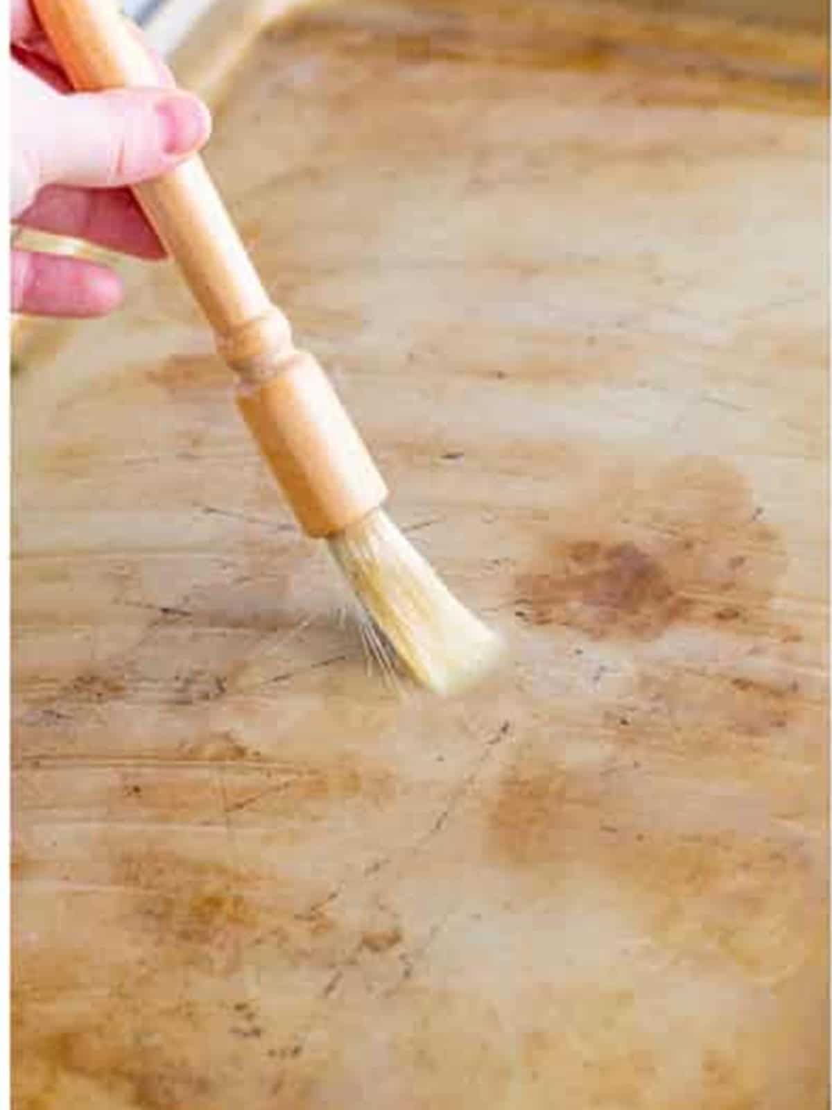 Brushing melted butter onto a sheet pan for sheet pan pancakes.
