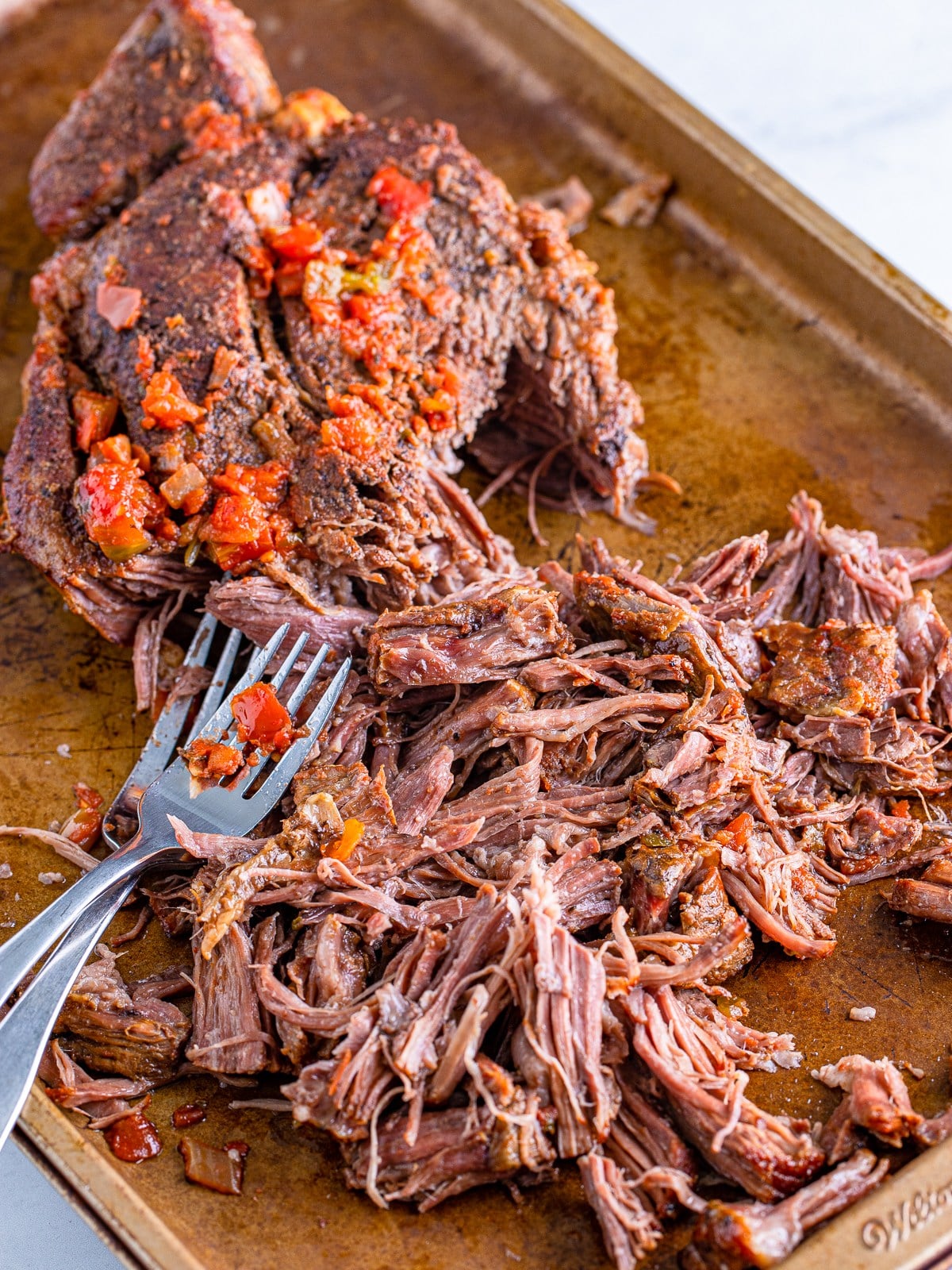 Shredding the cooked beef with two forks for shredded beef tacos.