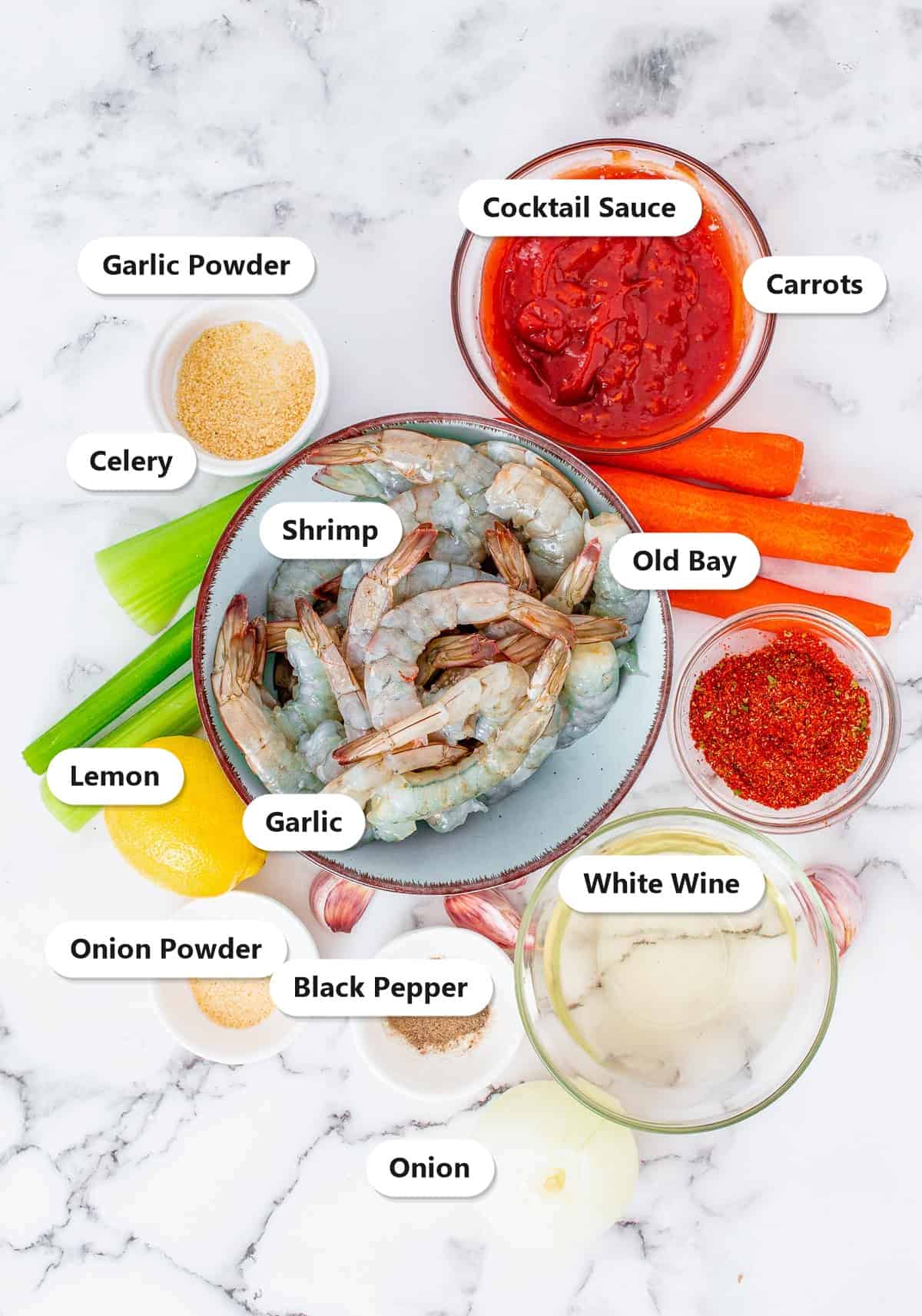 Labeled ingredients to make shrimp cocktail including raw shrimp, cocktail sauce, carrots, celery, lemon, garlic, onion, Old Bay, garlic powder, onion powder, black pepper, and white wine.