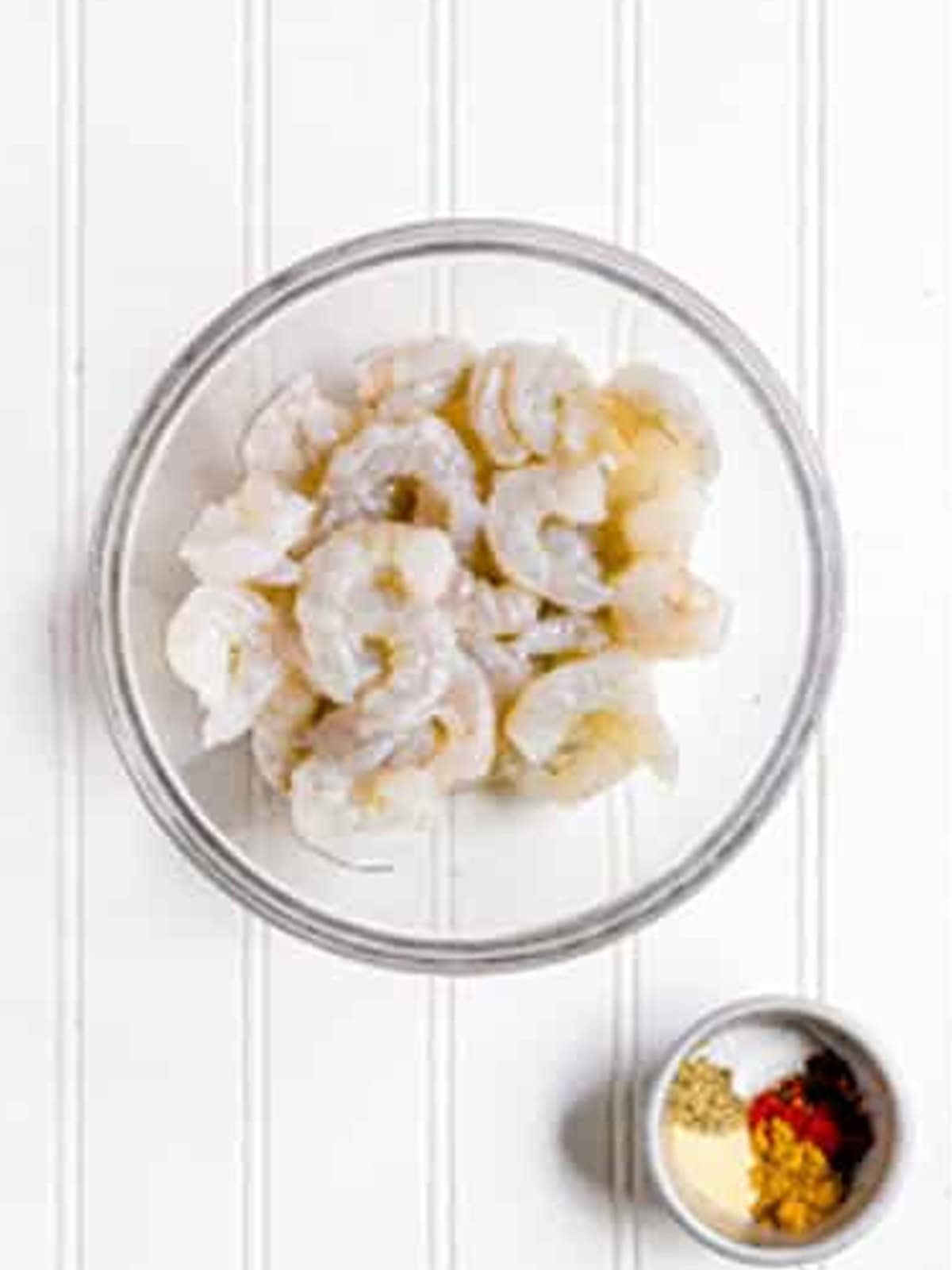 Raw shrimp in a bowl next to a small dish of taco seasoning for shrimp tacos.