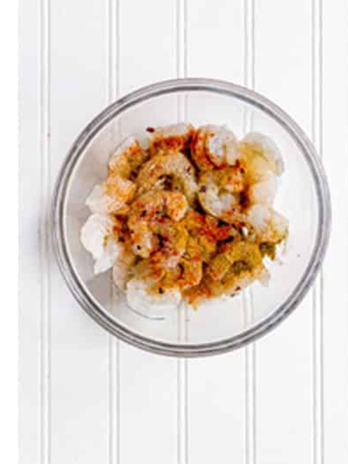 Shrimp tossed and coated in spicy taco seasoning in a glass bowl.