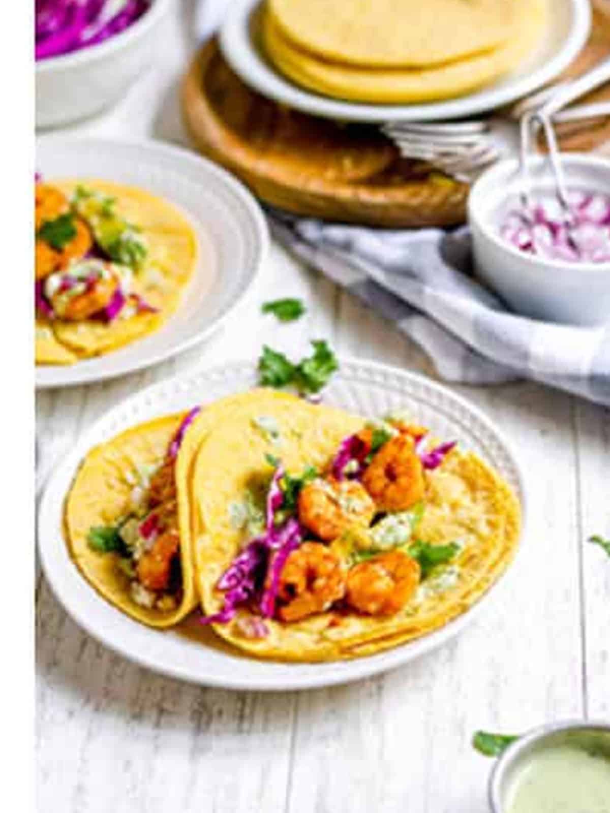 Assembled shrimp tacos on a plate topped with cabbage, avocado, and crema.