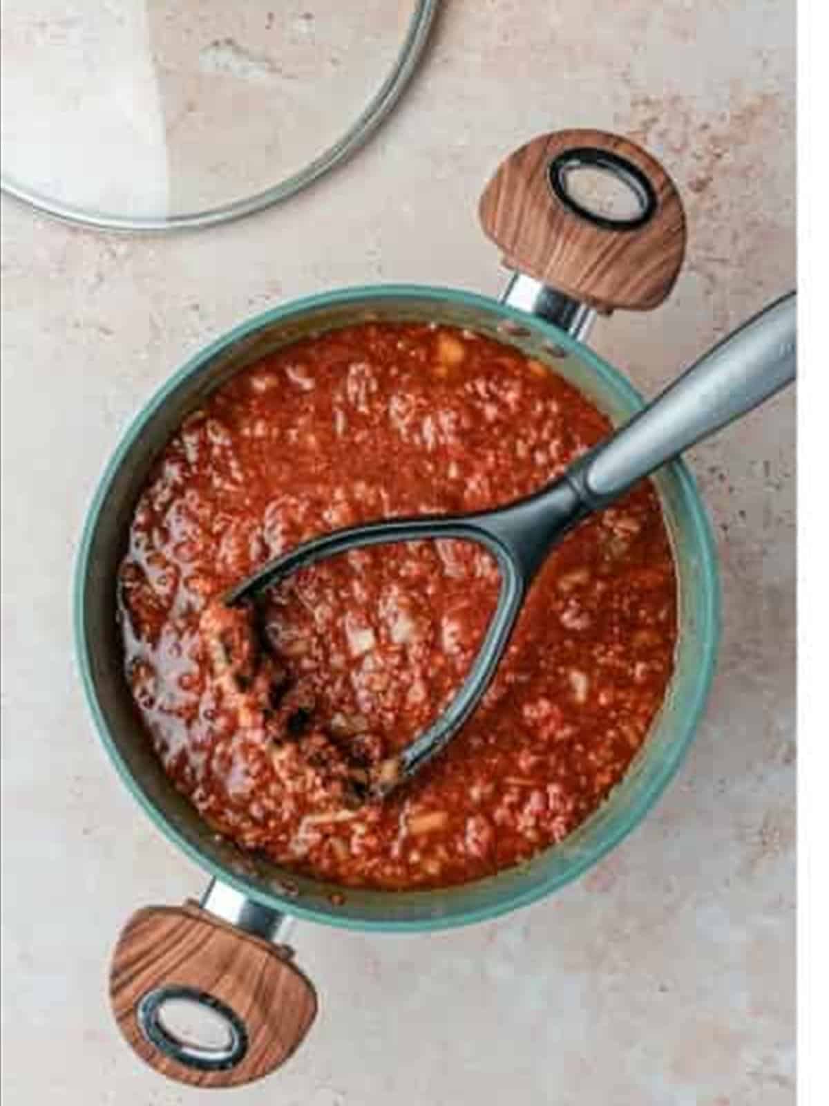 Mashing the beef with a potato masher for fine Skyline chili recipe texture.