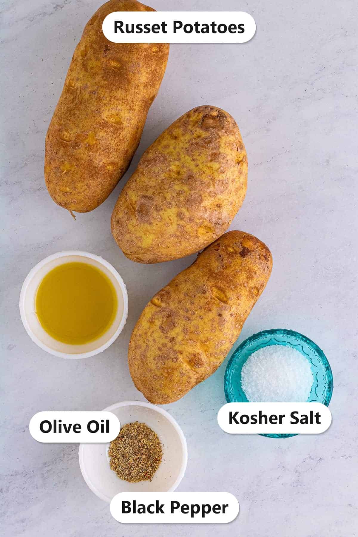 Labeled ingredients for slow cooker baked potatoes including russet potatoes, olive oil, kosher salt, and black pepper.
