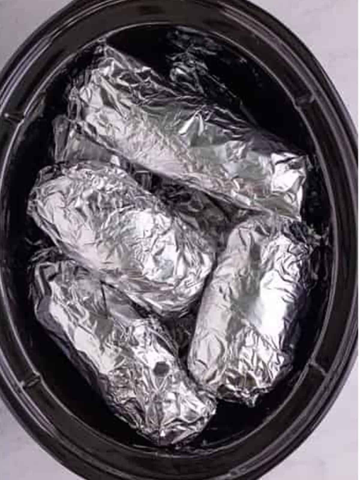 Foil wrapped potatoes stacked inside the slow cooker ready to cook.