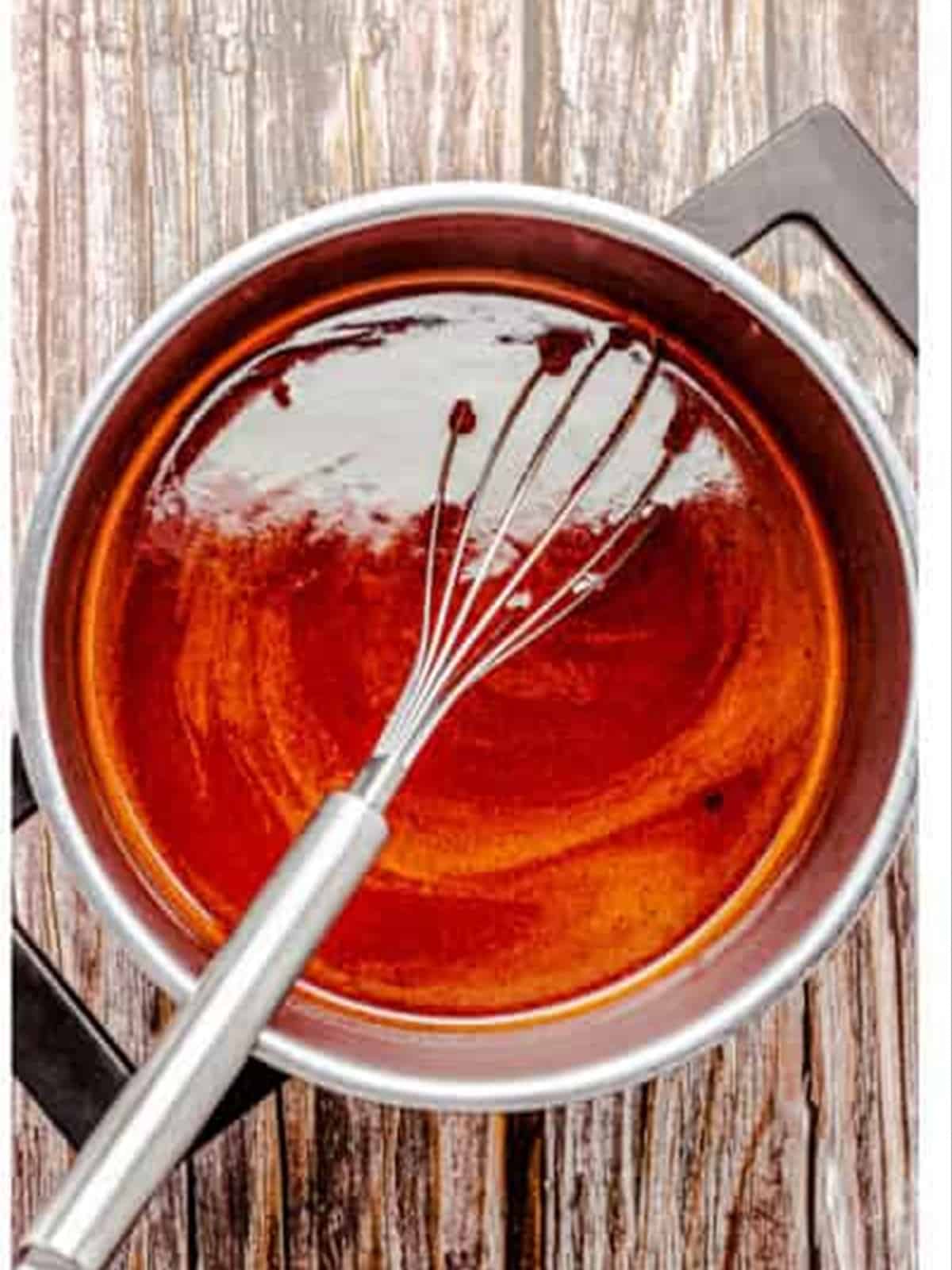 Whisking the homemade BBQ sauce in a saucepan for slow cooker BBQ chicken wings.