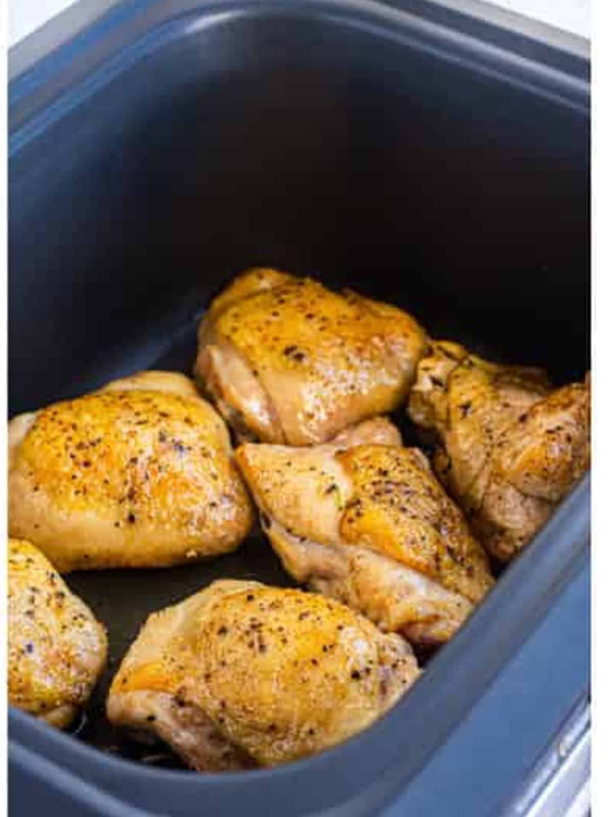 Seared chicken thighs arranged in the bottom of a slow cooker.