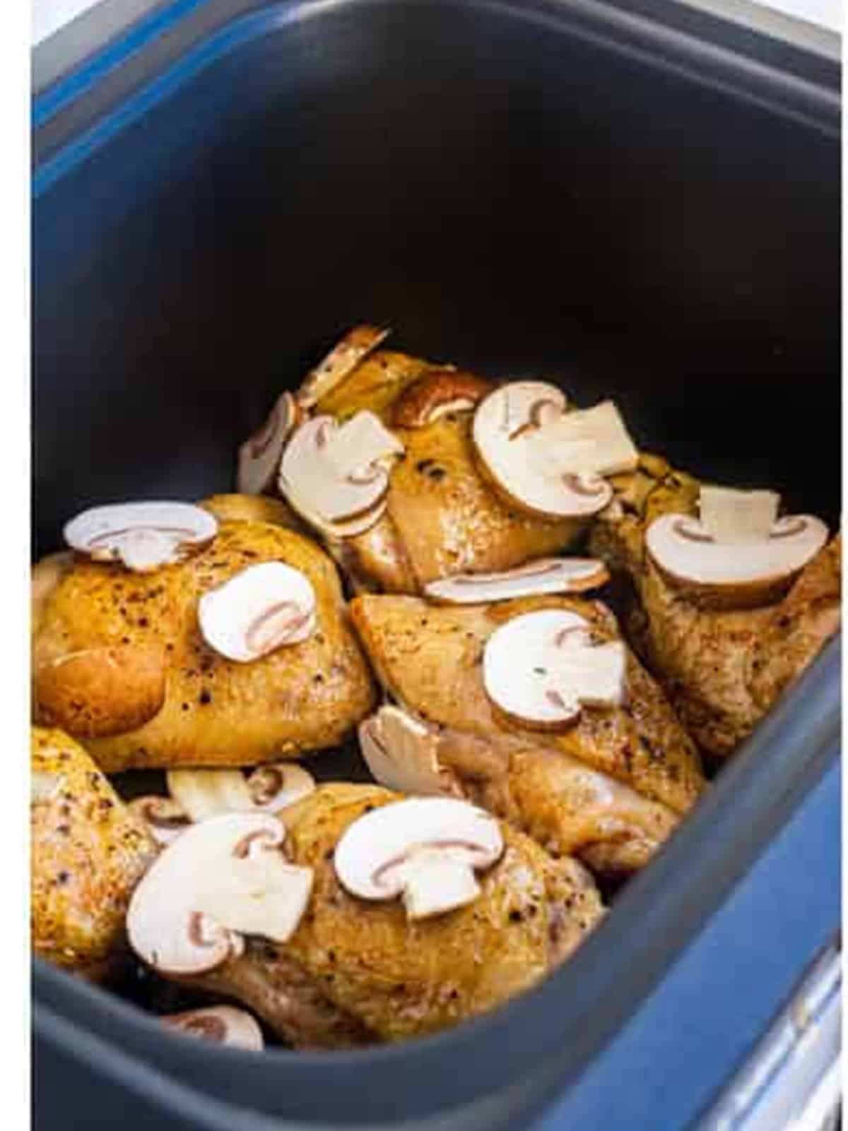 Sliced baby bella mushrooms added on top of the chicken thighs in the slow cooker.