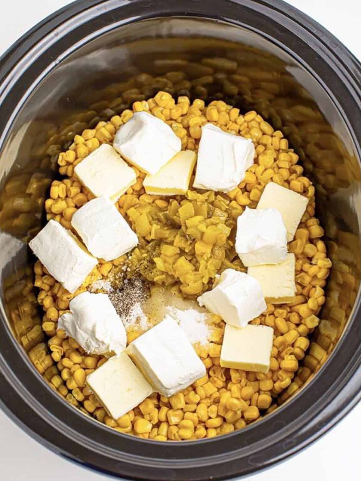 Corn topped with cubes of cream cheese, butter, diced green chiles, and seasonings in a slow cooker.
