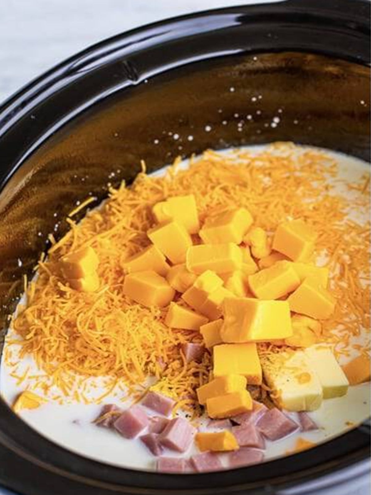 Diced ham, elbow macaroni, cheese, and butter added to a slow cooker for mac and cheese.