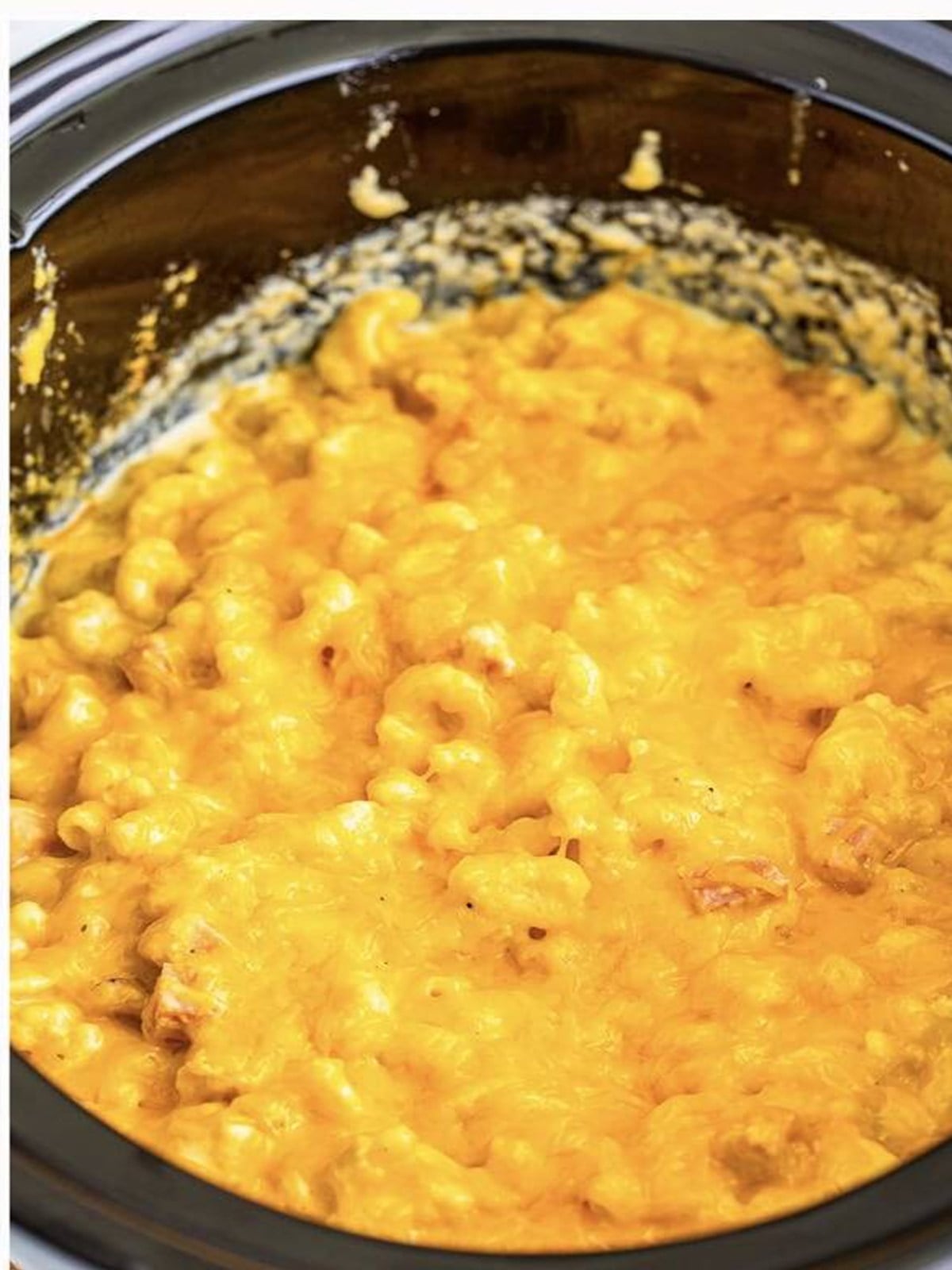 Finished cheesy slow cooker mac and cheese with ham topped with melted cheddar.