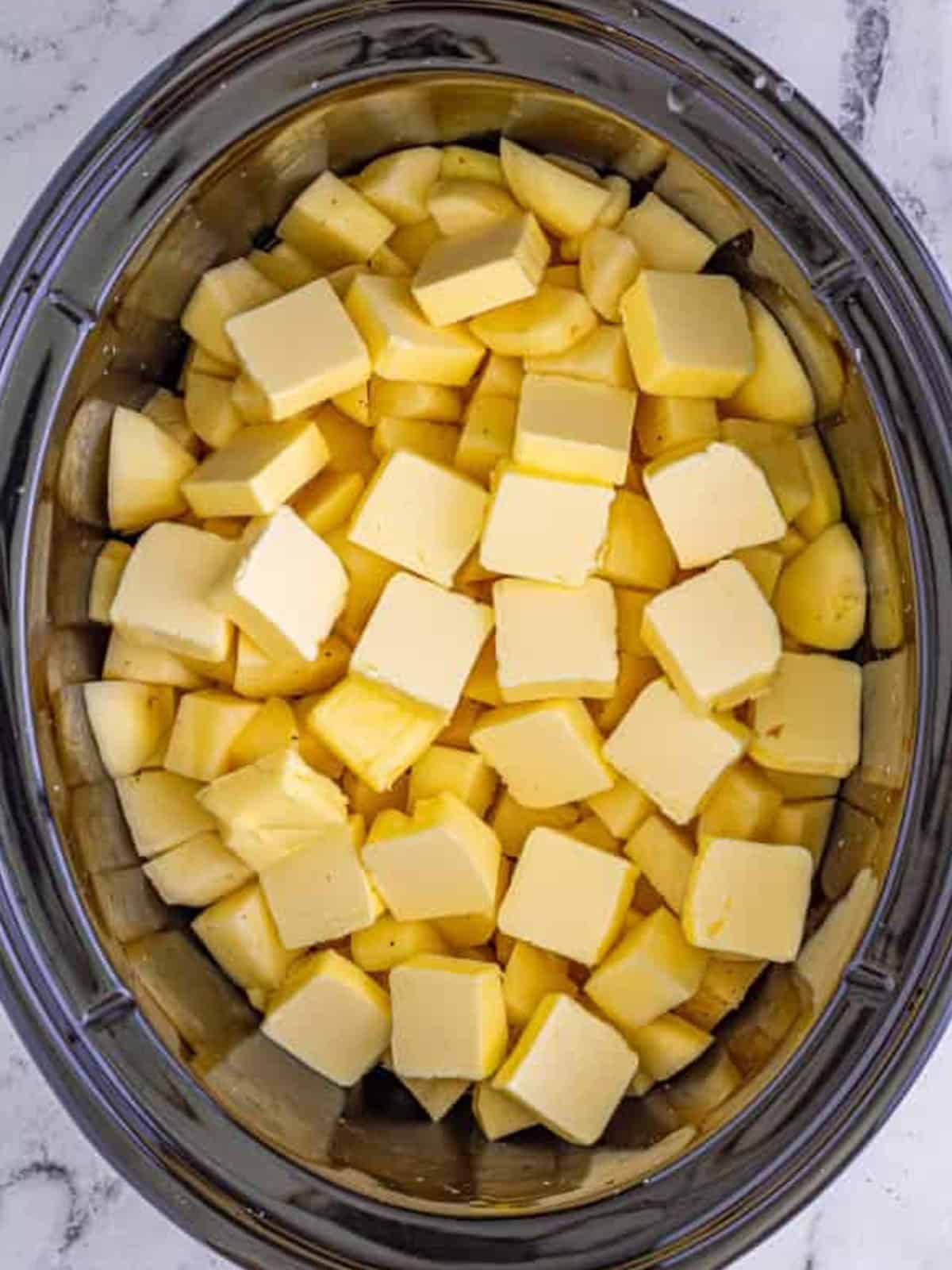 Sliced butter placed on top of diced potatoes in a slow cooker before cooking.