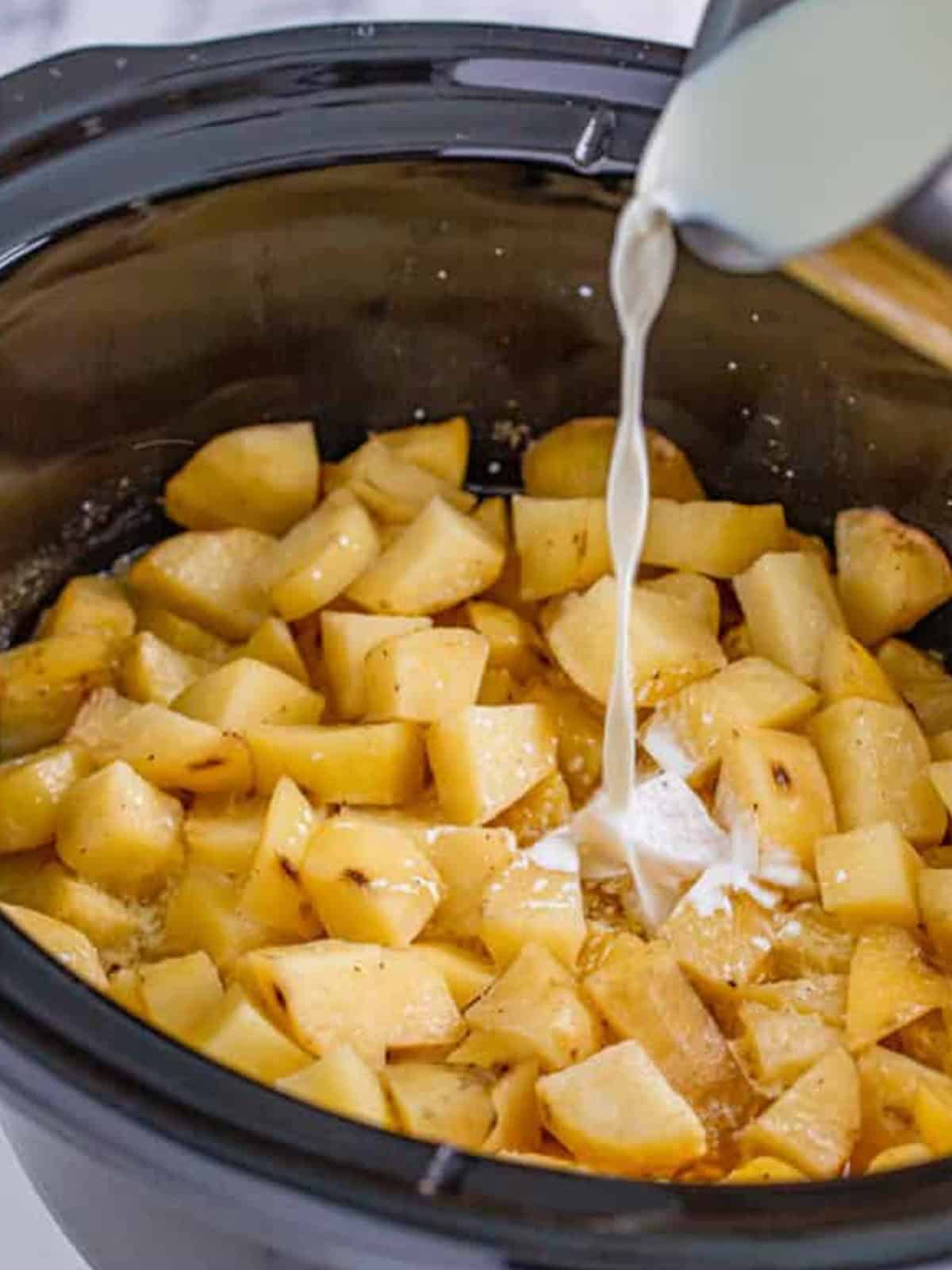 Pouring warm half and half over the cooked potatoes in the slow cooker.