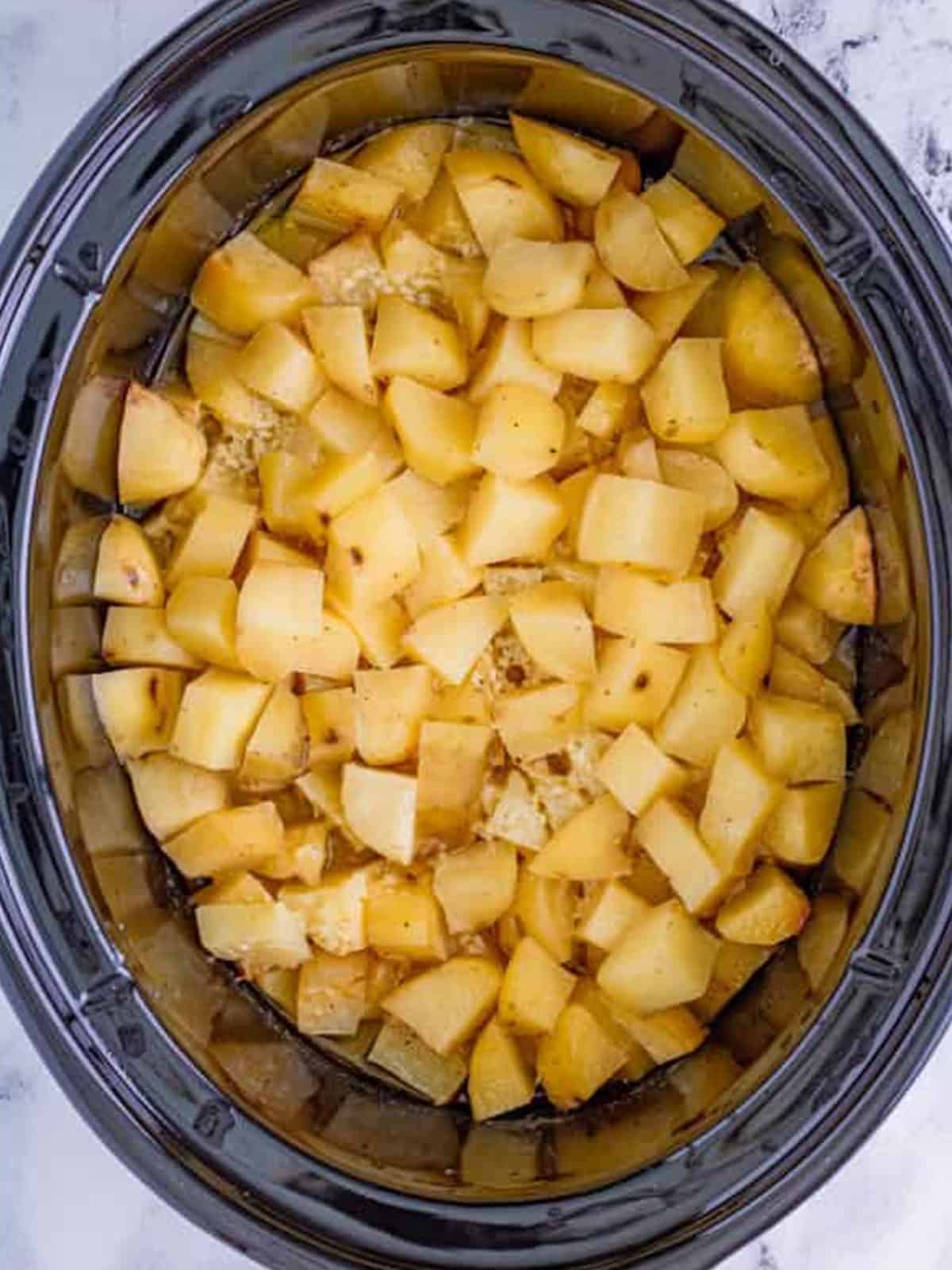 Diced russet potatoes with garlic, stock, salt, and pepper in a slow cooker.