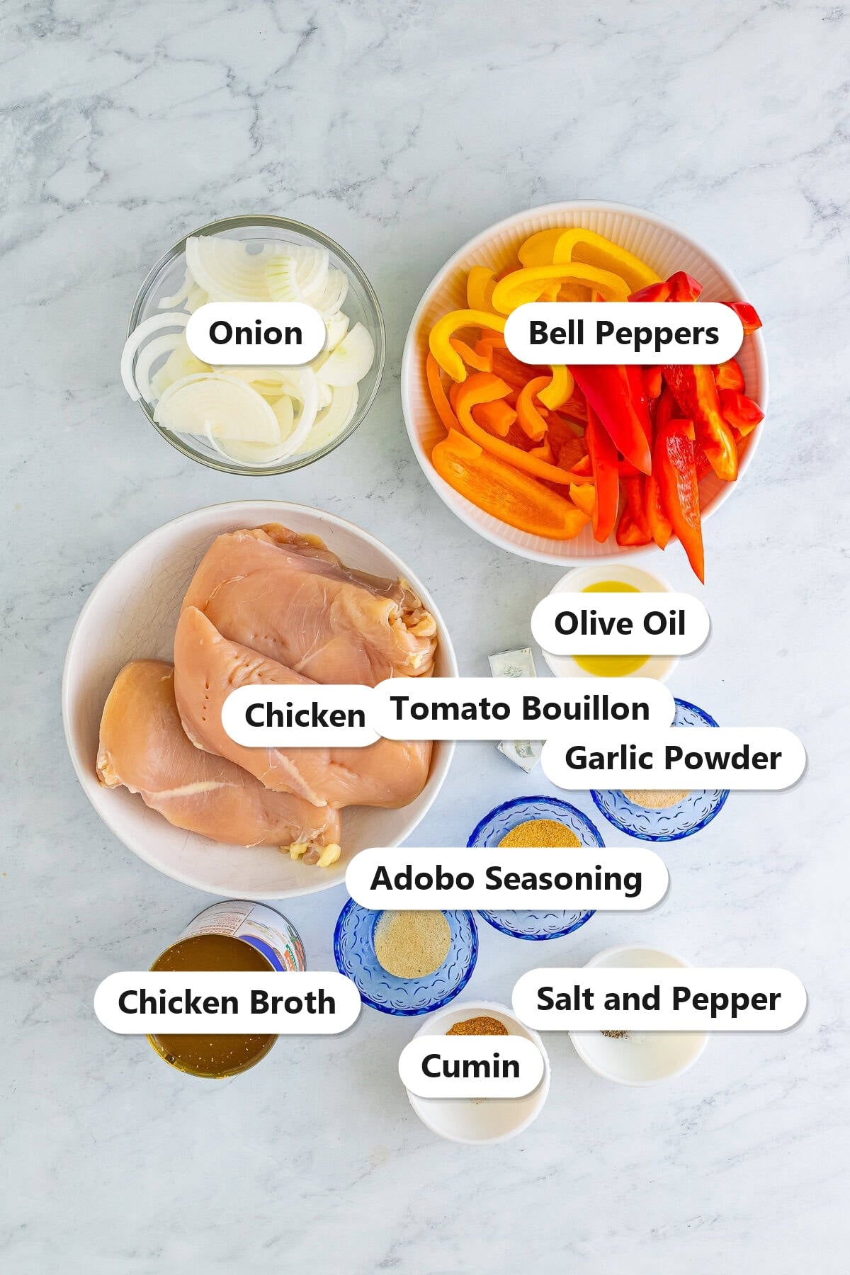 Labeled ingredients to make slow cooker shredded chicken including chicken breast, bell peppers, onion, olive oil, tomato bouillon, garlic powder, adobo seasoning, cumin, salt, pepper, and chicken broth.