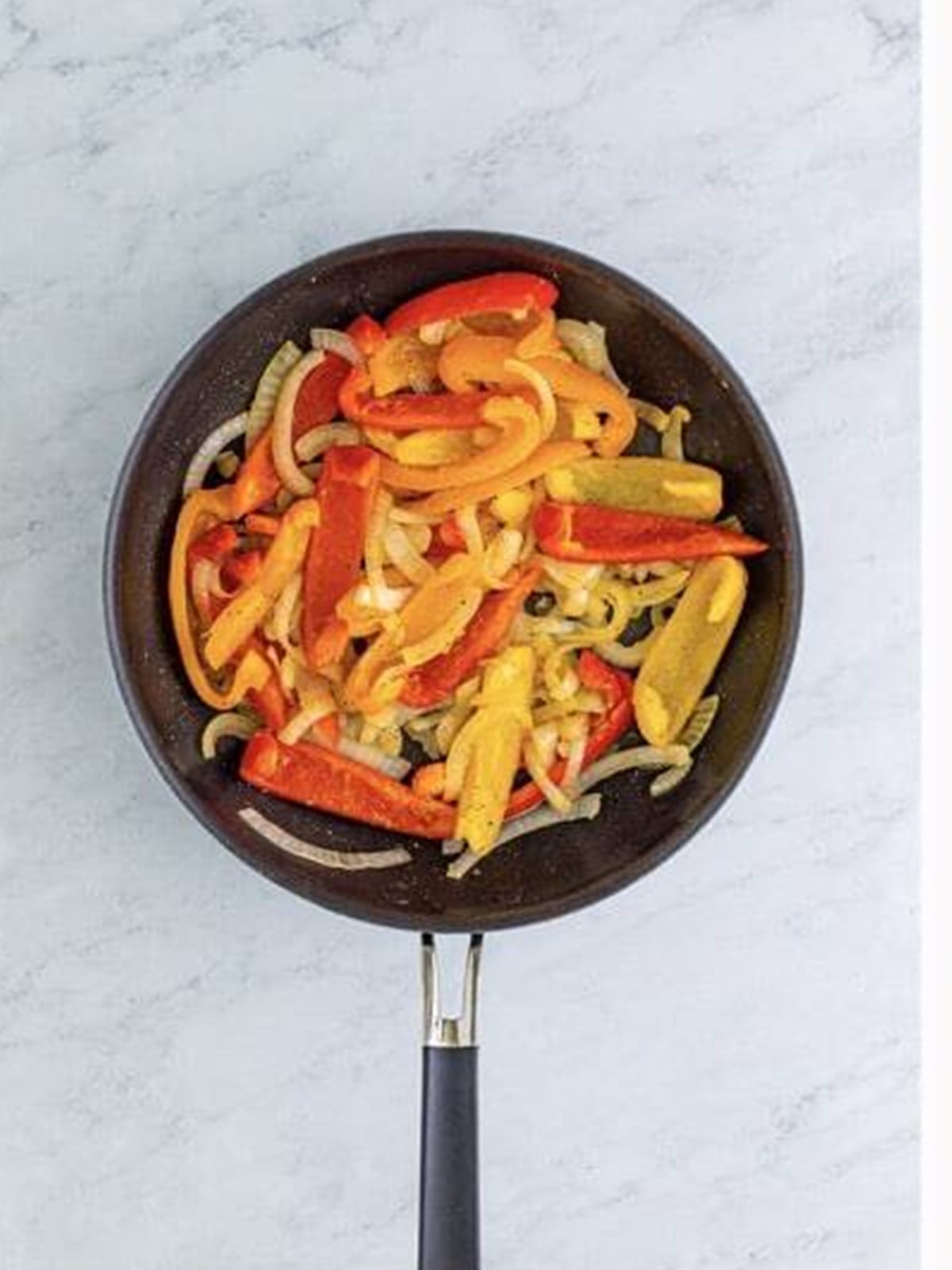 Bell peppers and onion sauteing in a skillet for slow cooker shredded chicken.