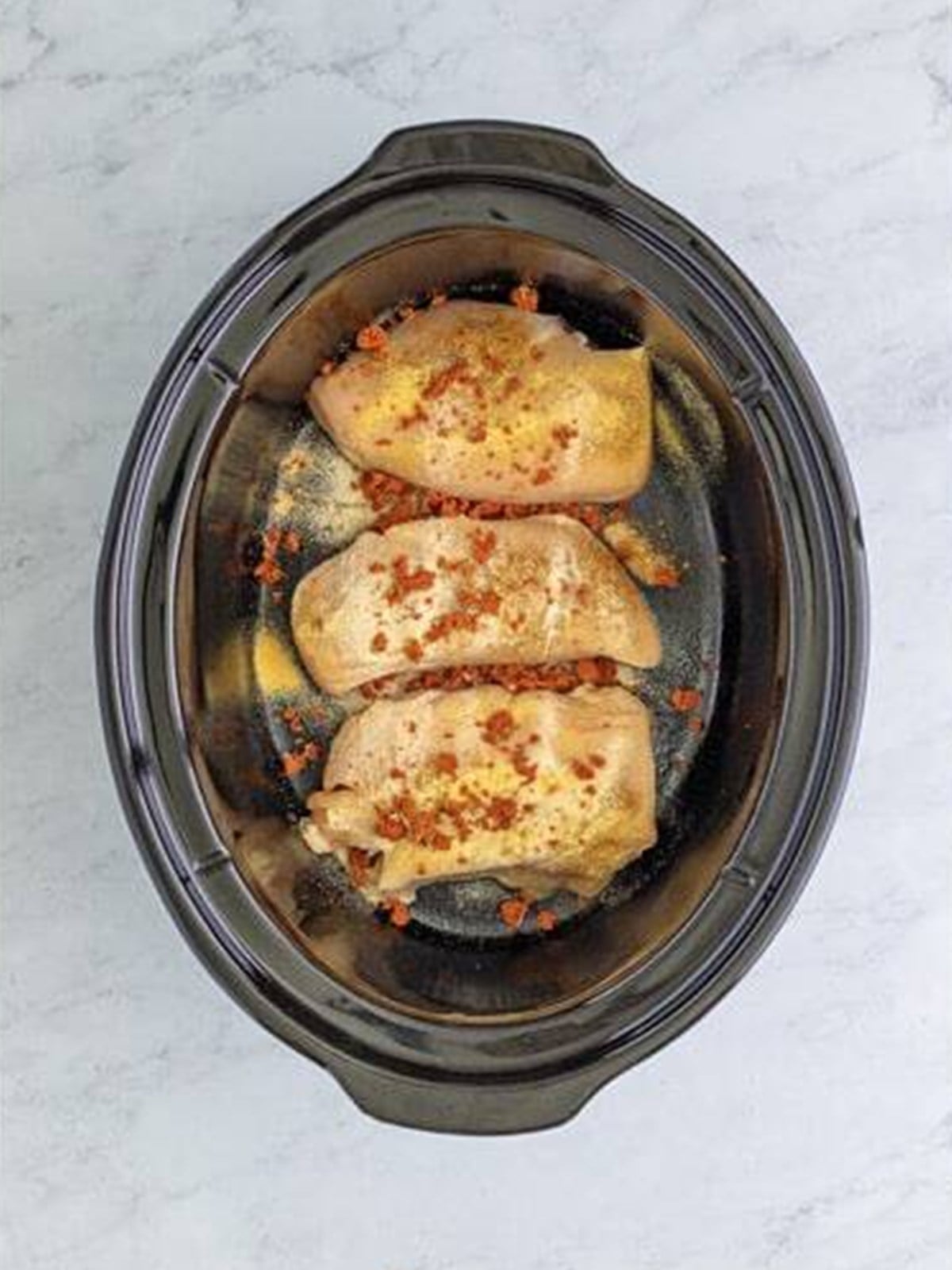 Raw chicken breasts seasoned in the bottom of a slow cooker.