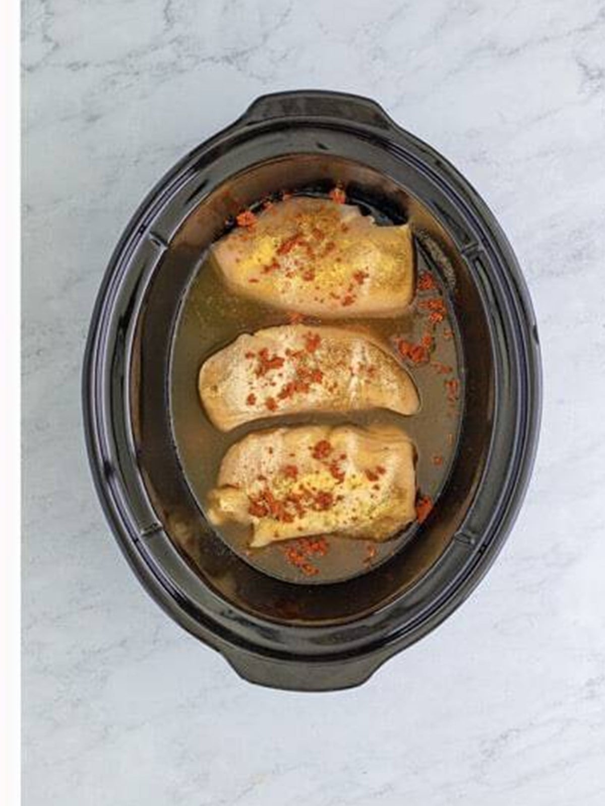 Seasoned chicken with broth poured around it in the slow cooker.
