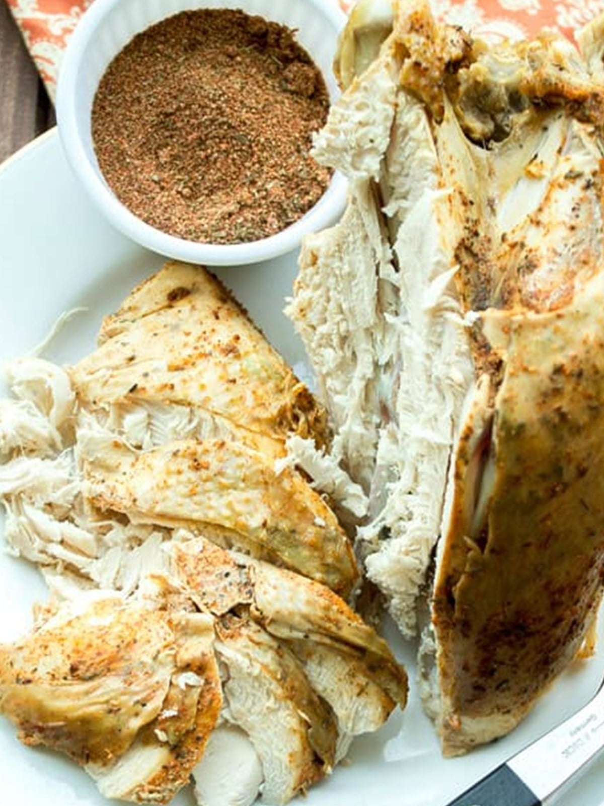 Sliced slow cooker Cajun turkey breast on a platter next to a bowl of homemade Cajun seasoning blend.