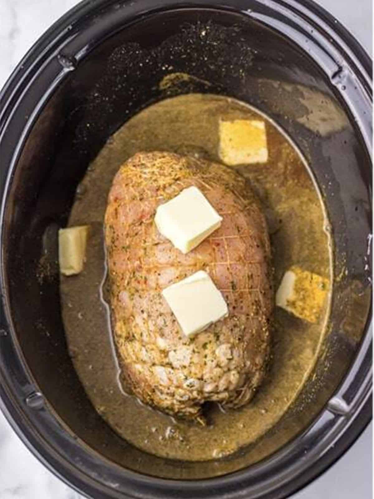 A turkey breast in a slow cooker topped with pats of butter and gravy.