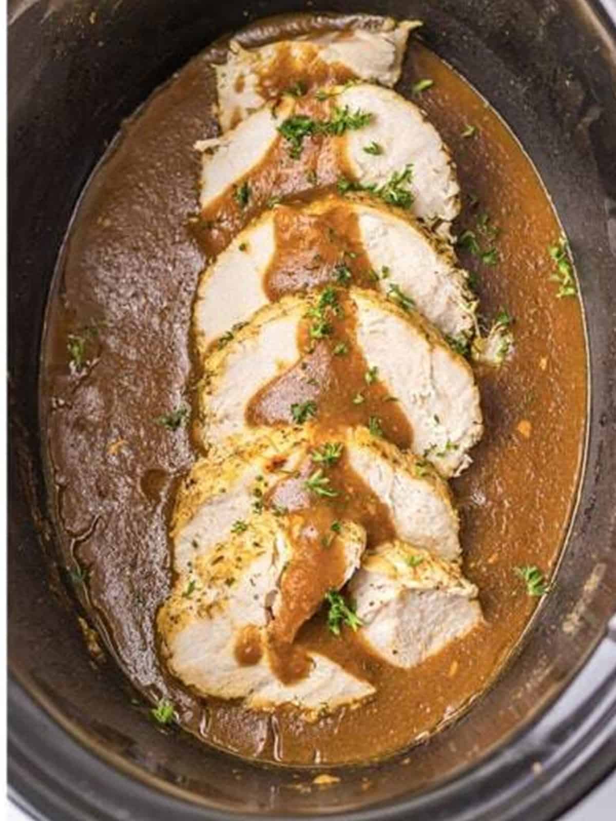 Sliced slow cooker turkey breast in rich gravy in the crock.