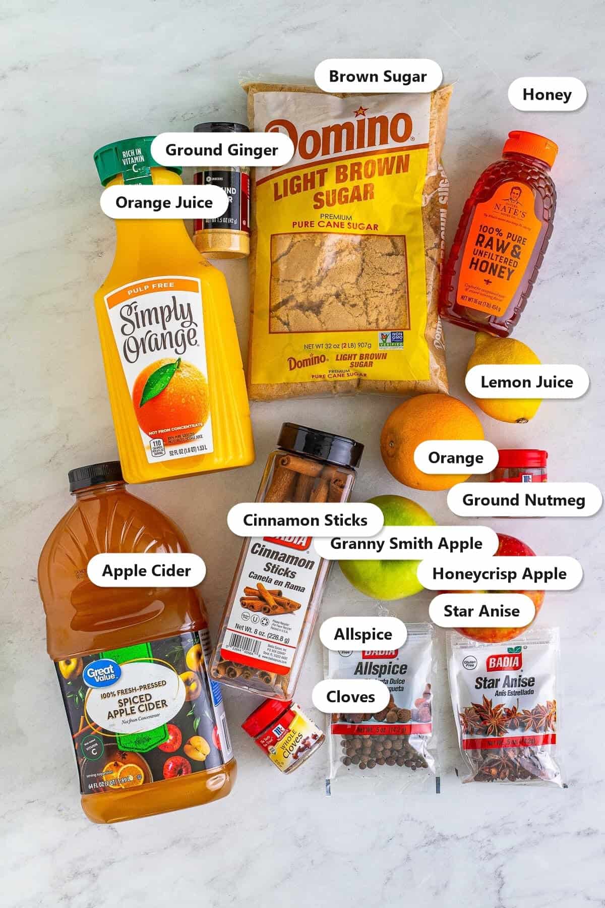 Labeled ingredients to make slow cooker wassail including apple cider, orange juice, brown sugar, honey, and warm spices.