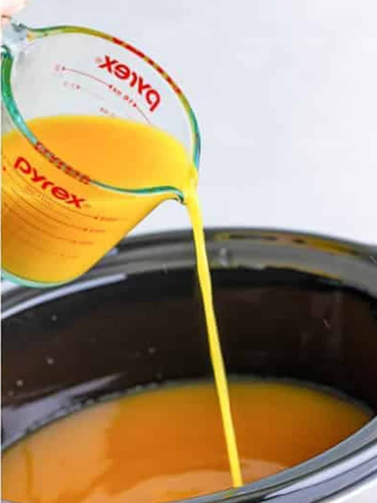 Orange juice being poured into the slow cooker with the apple cider.