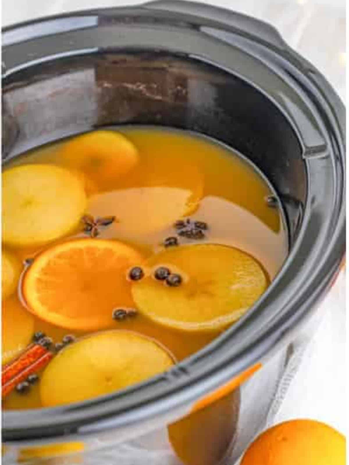 Finished slow cooker wassail with floating apple and orange slices and warm spices.